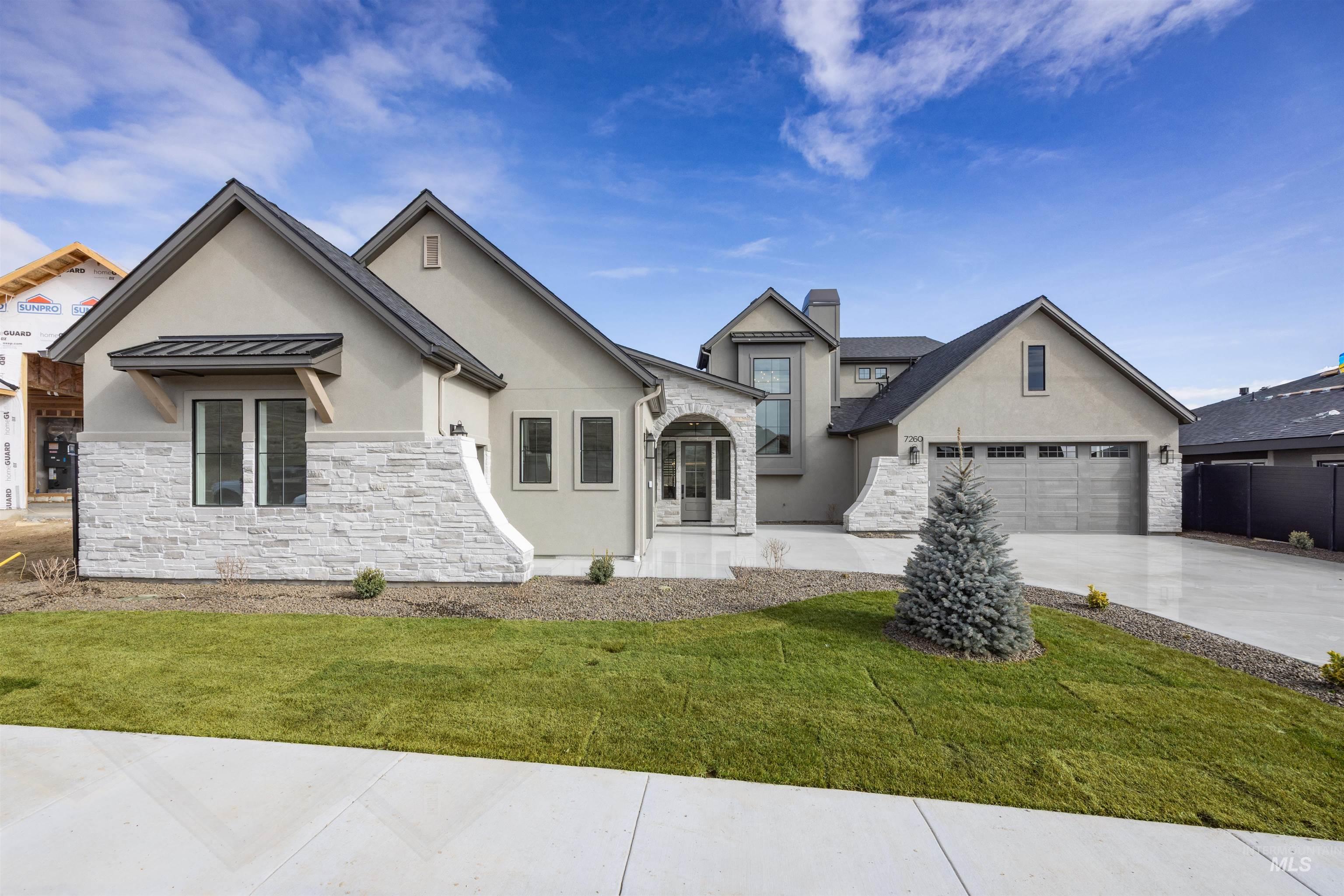 View of front of home with stucco siding, stone siding, a front yard, driveway, and a chimney