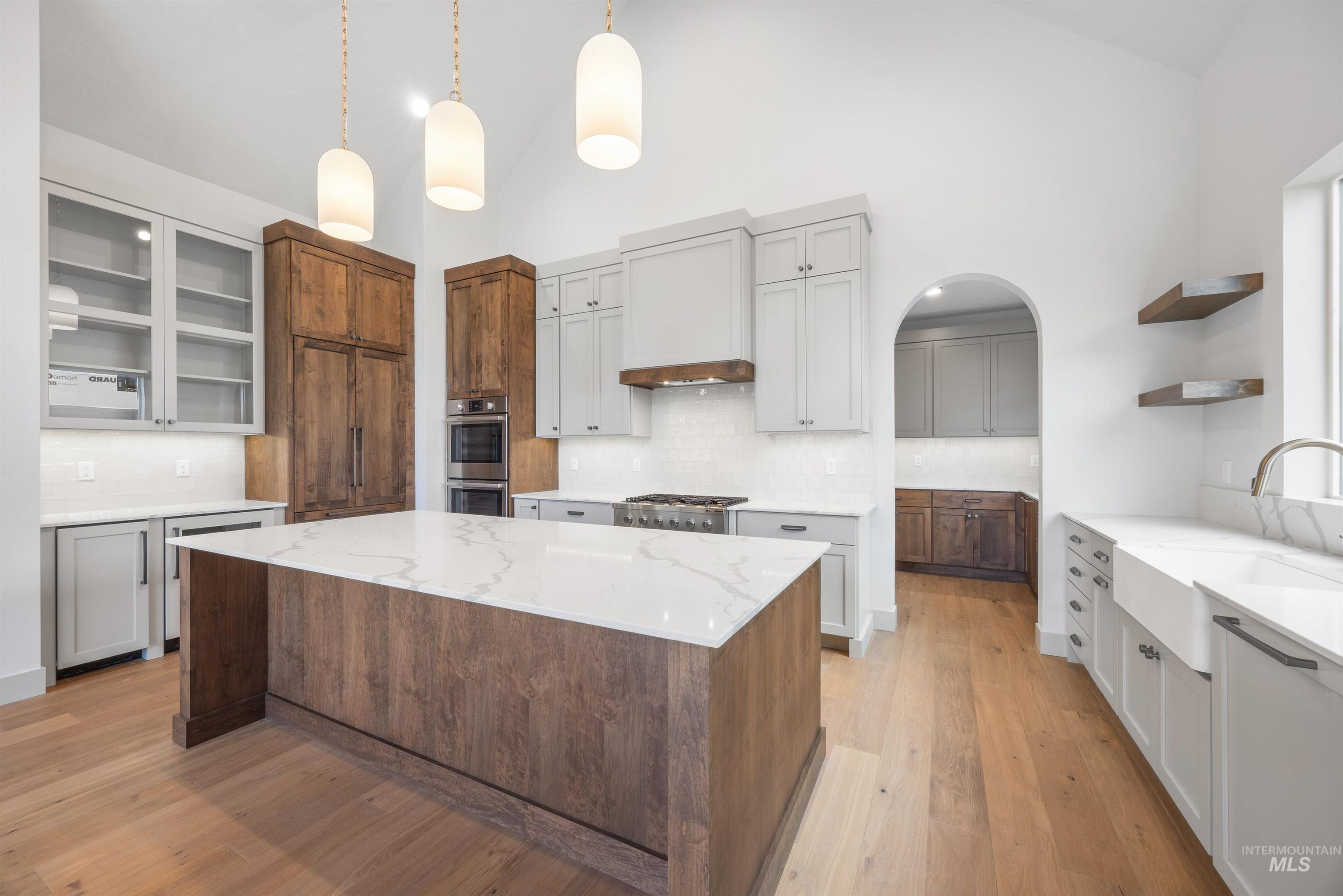 Dual tone kitchen with open shelves, a kitchen island, light stone counters, two tone cabinets, and glass fronted cabinets