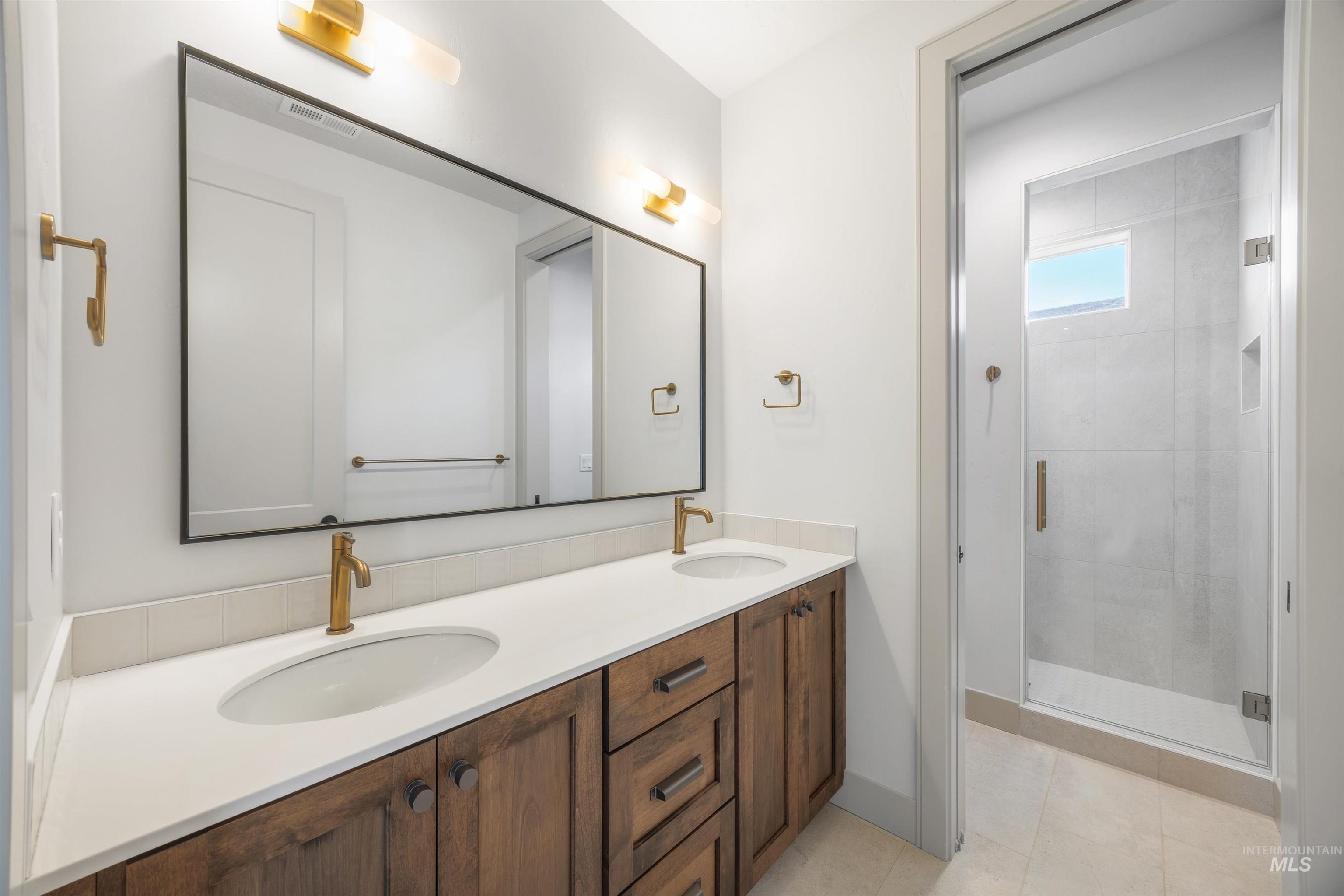 Full bath with double vanity, a shower stall, and light tile patterned flooring