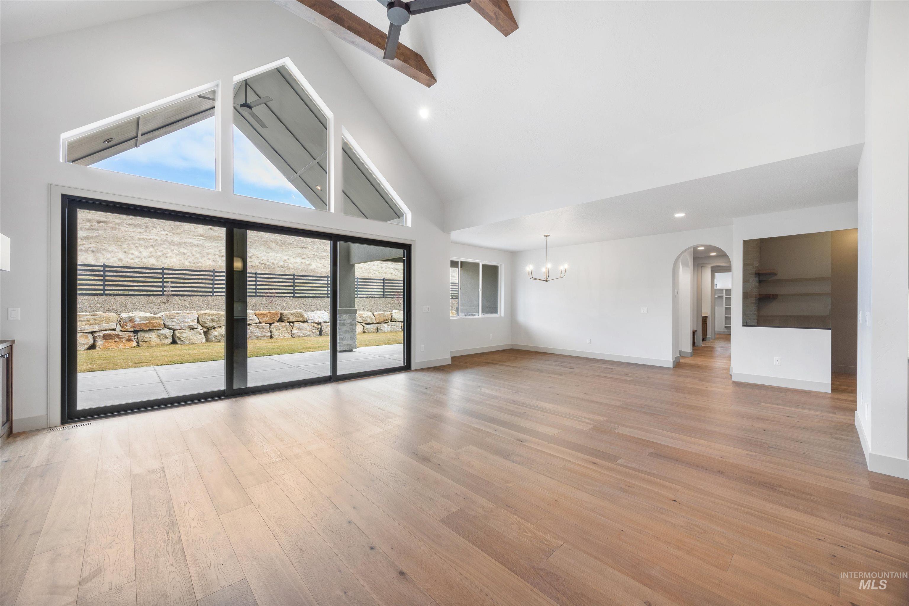 Unfurnished living room with arched walkways, lofted ceiling, light wood-style floors, and suspended lighting