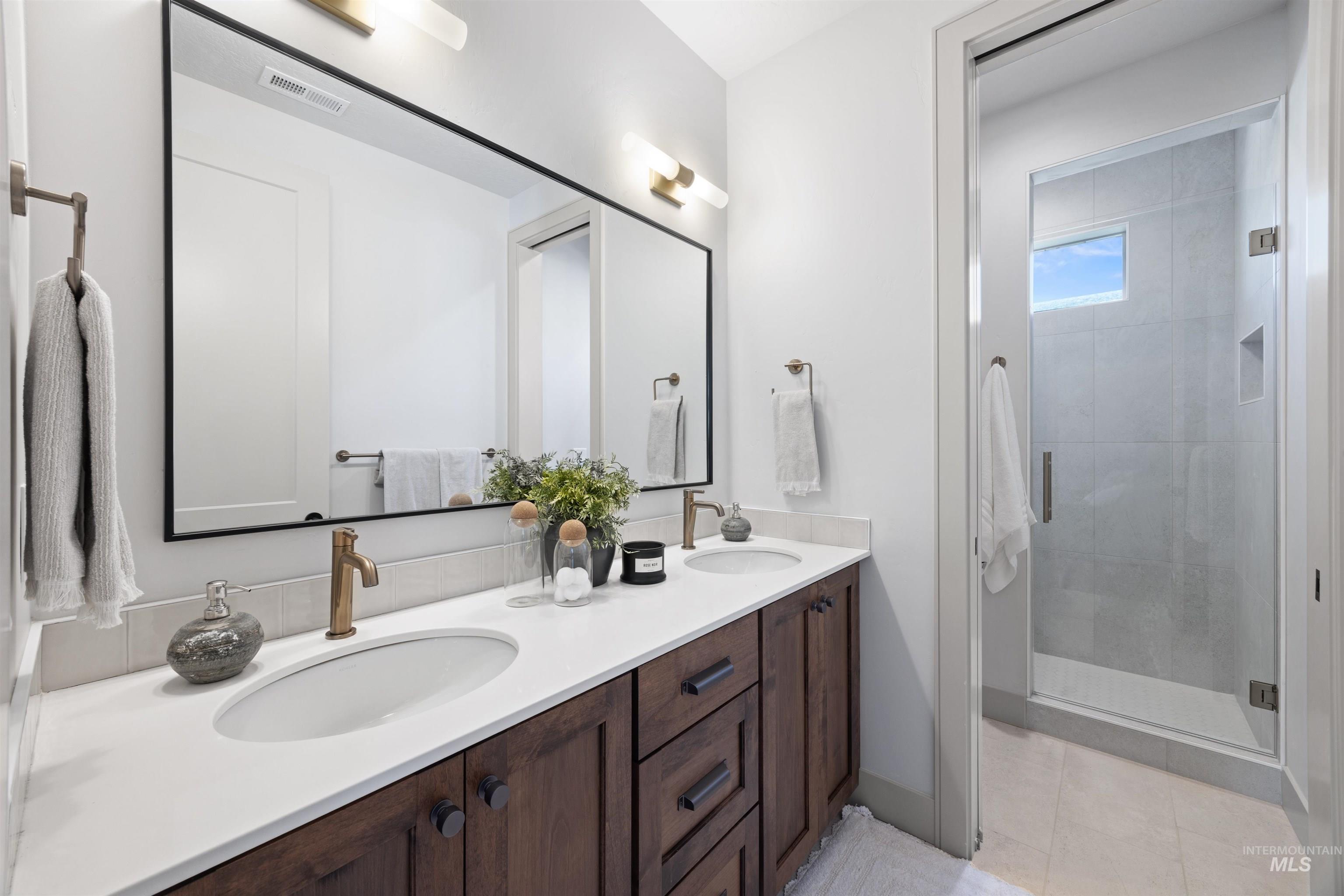 Full bath with double vanity, a stall shower, and light tile patterned floors