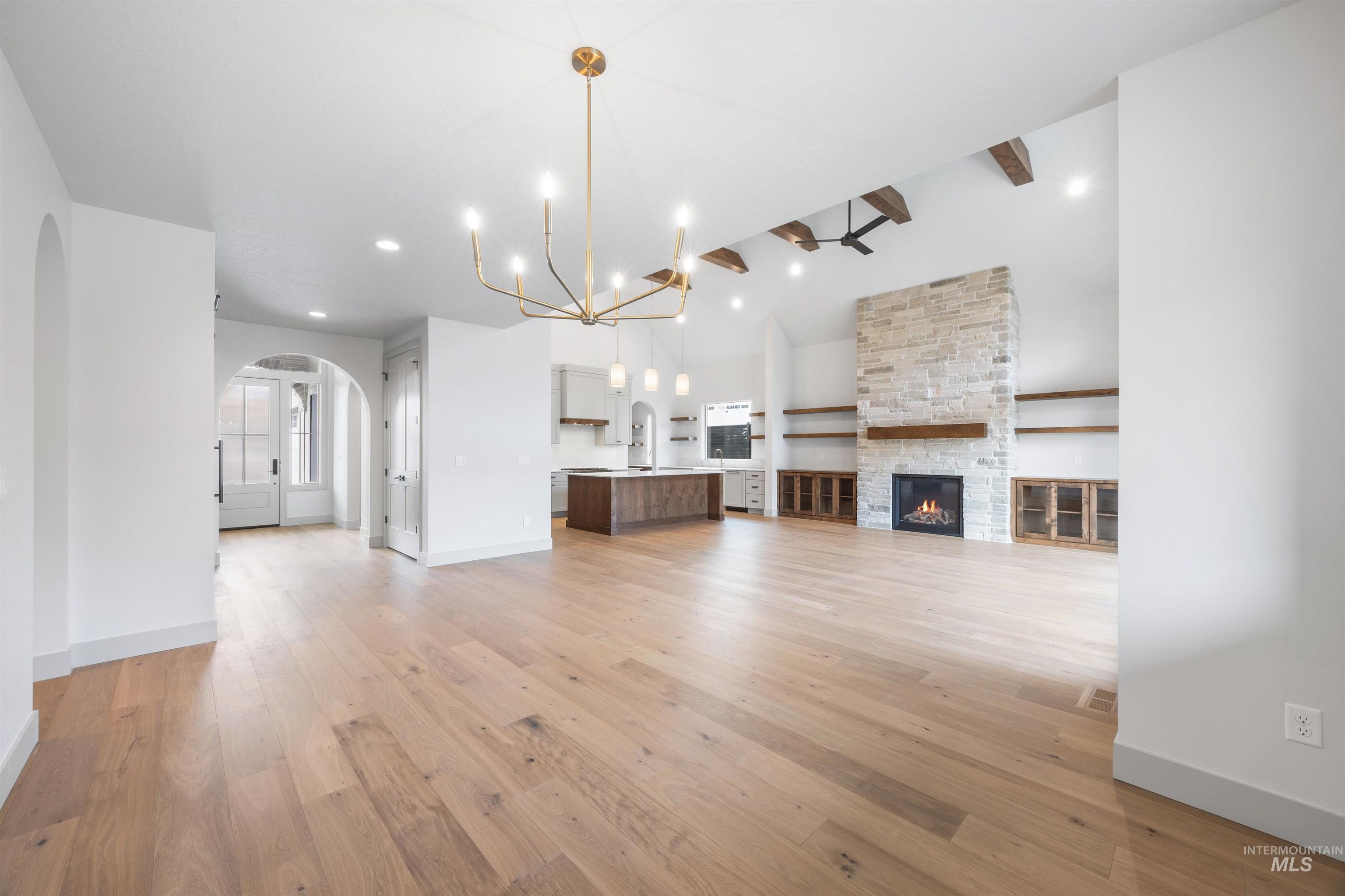 Unfurnished living room featuring suspended lighting, a stone fireplace, arched walkways, light wood-style floors, and lofted ceiling