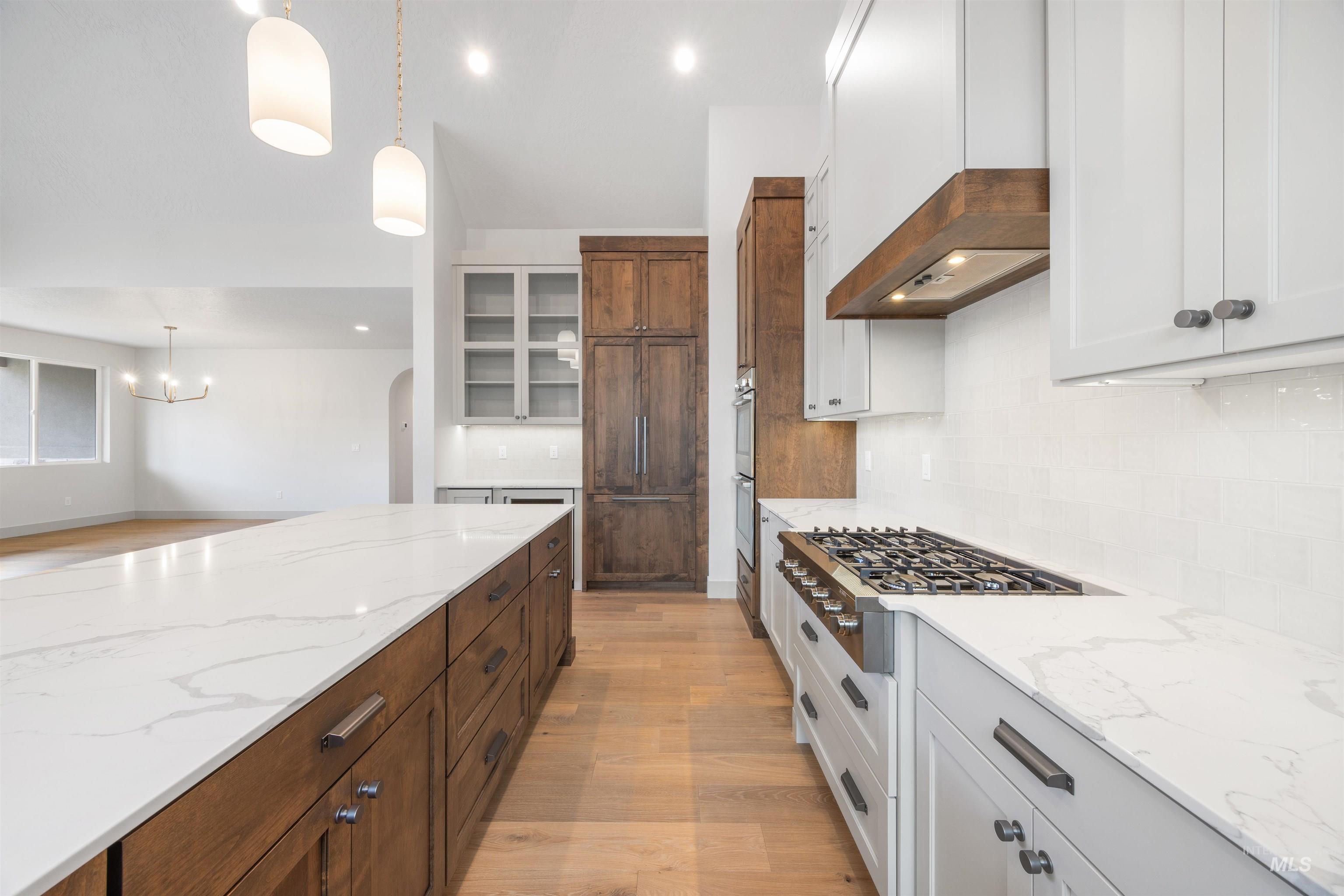 Dual tone kitchen featuring two tone color scheme, light stone countertops, stainless steel appliances, light wood-style floors, and tasteful backsplash