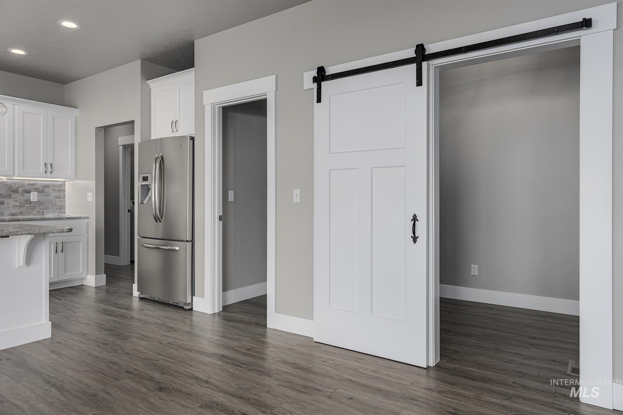 Kitchen featuring white cabinetry, a barn door, stainless steel fridge, light stone countertops, and recessed lighting