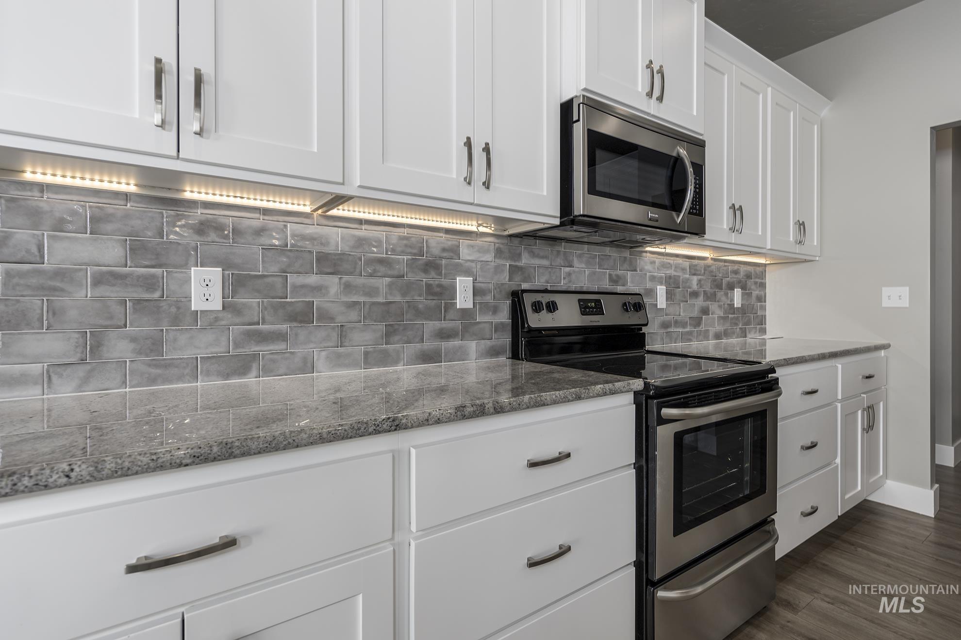Kitchen featuring stainless steel appliances, white cabinetry, dark stone countertops, dark wood-style floors, and decorative backsplash