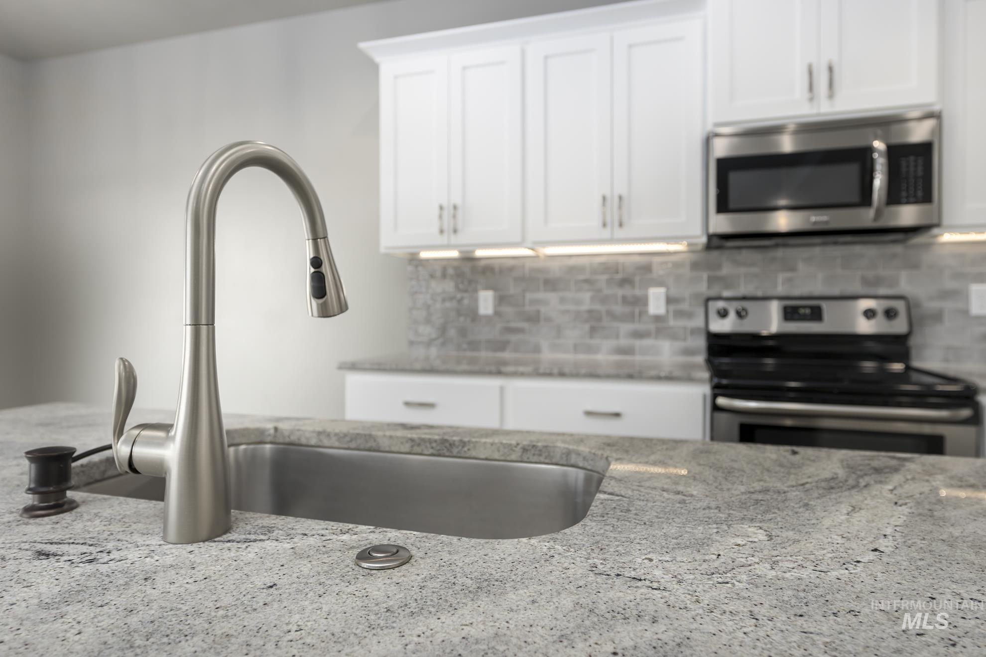 Kitchen featuring stainless steel appliances, light stone countertops, white cabinetry, and decorative backsplash