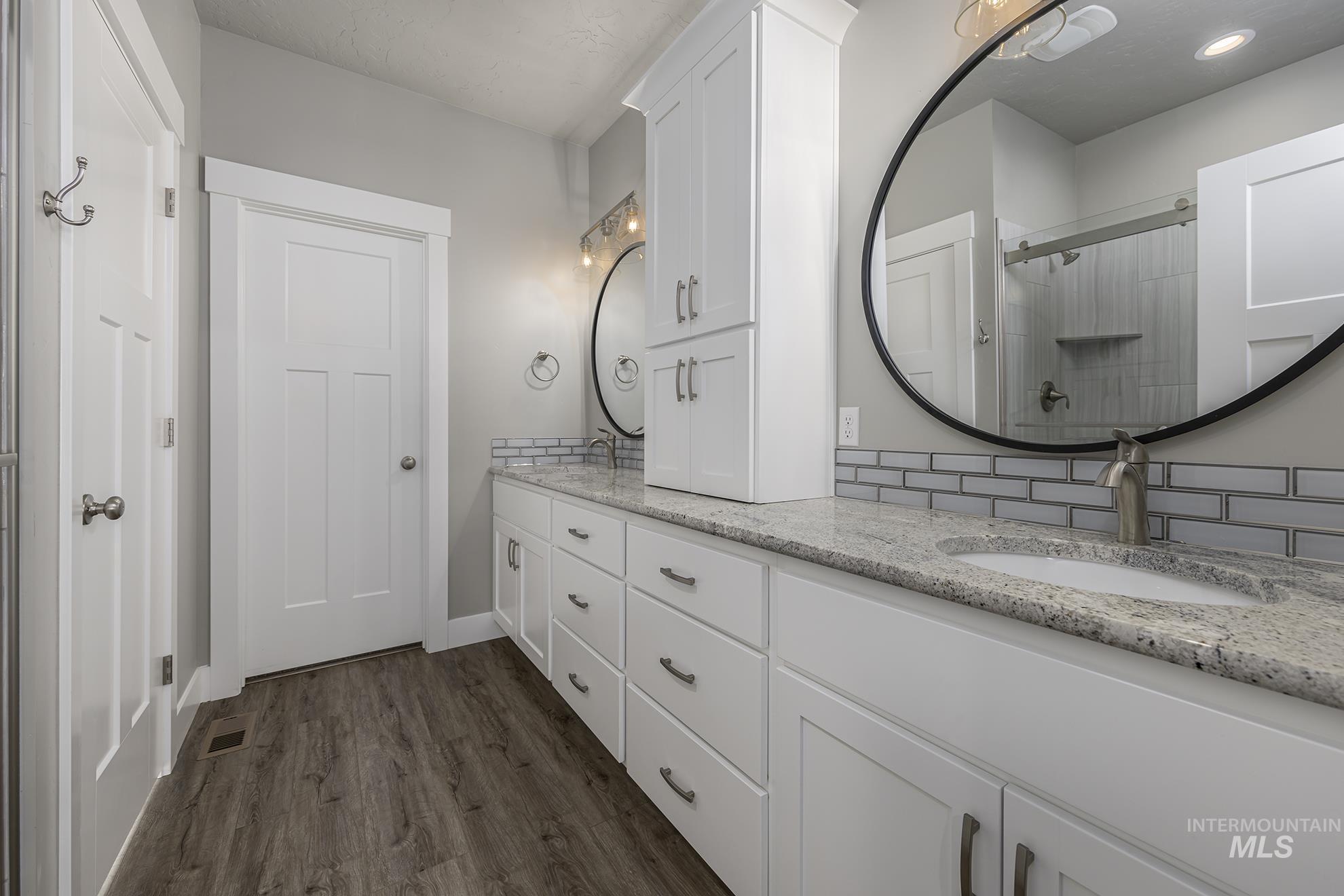 Full bathroom with double vanity, dark wood-style floors, and a stall shower