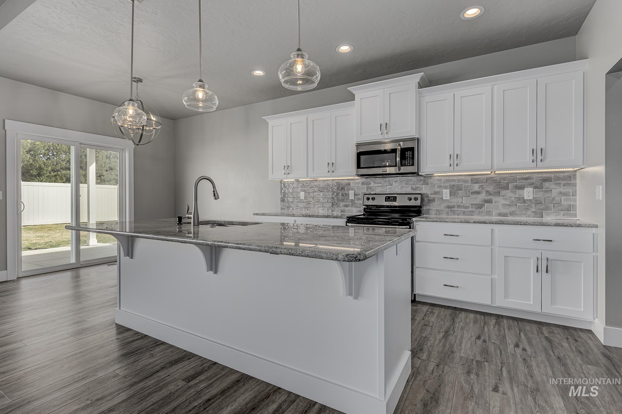 Kitchen featuring white cabinets, a breakfast bar area, light stone countertops, a center island with sink, and stainless steel appliances