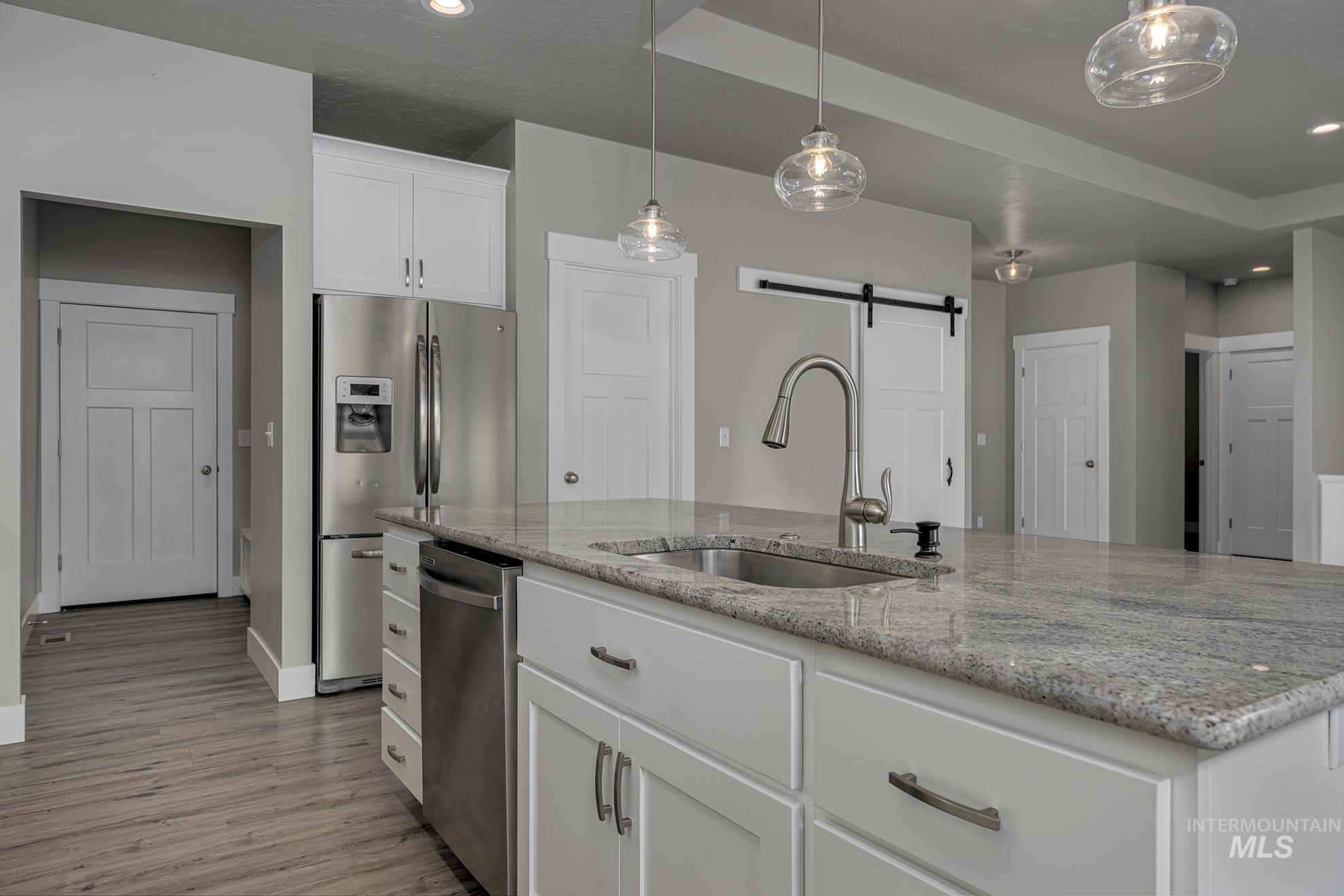 Kitchen with white cabinets, a barn door, stainless steel appliances, light stone countertops, and a kitchen island with sink