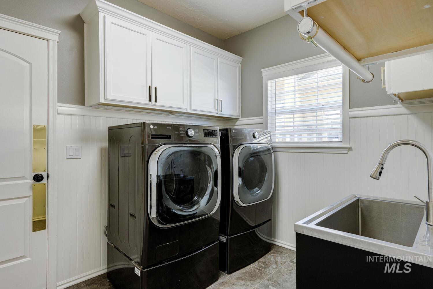Washroom featuring wainscoting, cabinet space, wooden walls, and washing machine and clothes dryer
