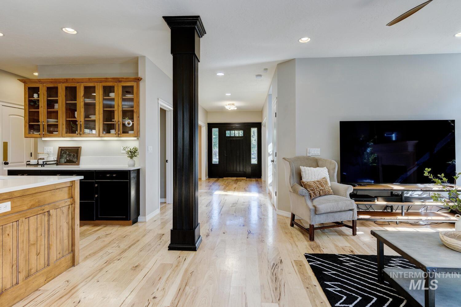 Bar featuring recessed lighting, light wood-style flooring, glass insert cabinets, brown cabinetry, and decorative columns