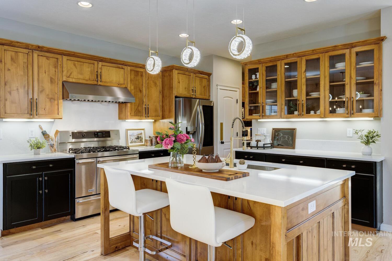 Kitchen with appliances with stainless steel finishes, an island with sink, under cabinet range hood, brown cabinetry, and recessed lighting