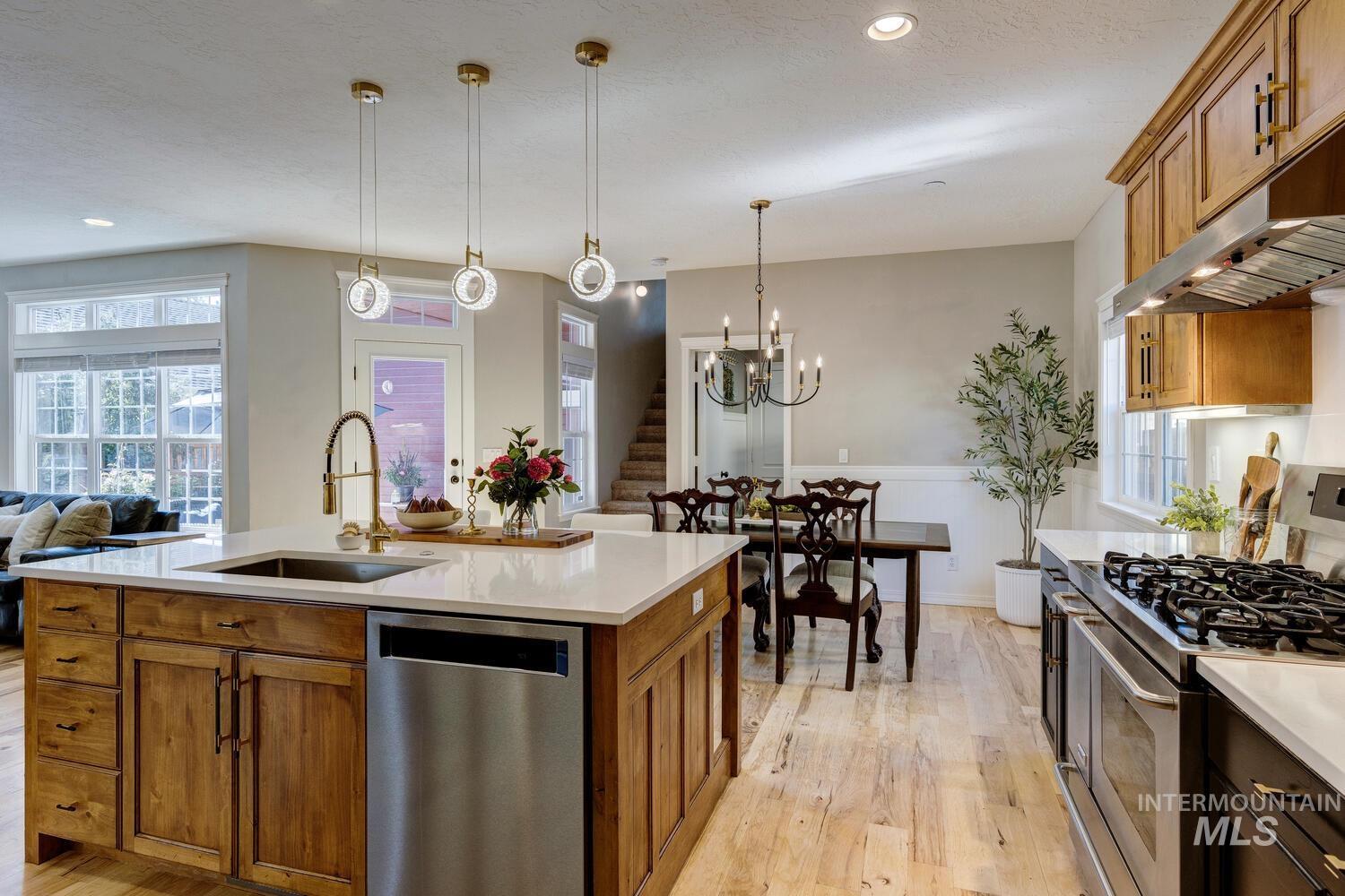 Kitchen with appliances with stainless steel finishes, brown cabinets, pendant lighting, light wood-style flooring, and open floor plan
