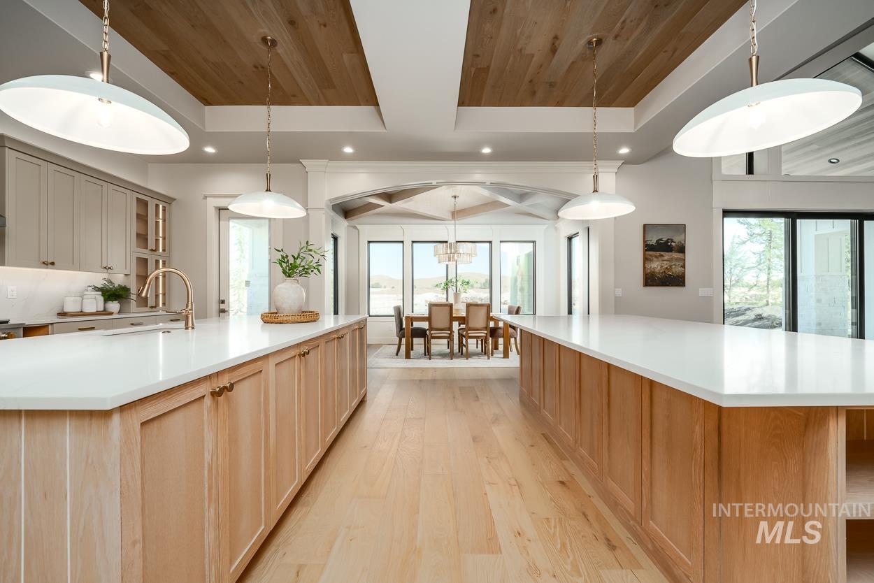 Kitchen featuring a spacious island, light wood-style flooring, pendant lighting, light stone counters, and a wood ceiling with exposed beams