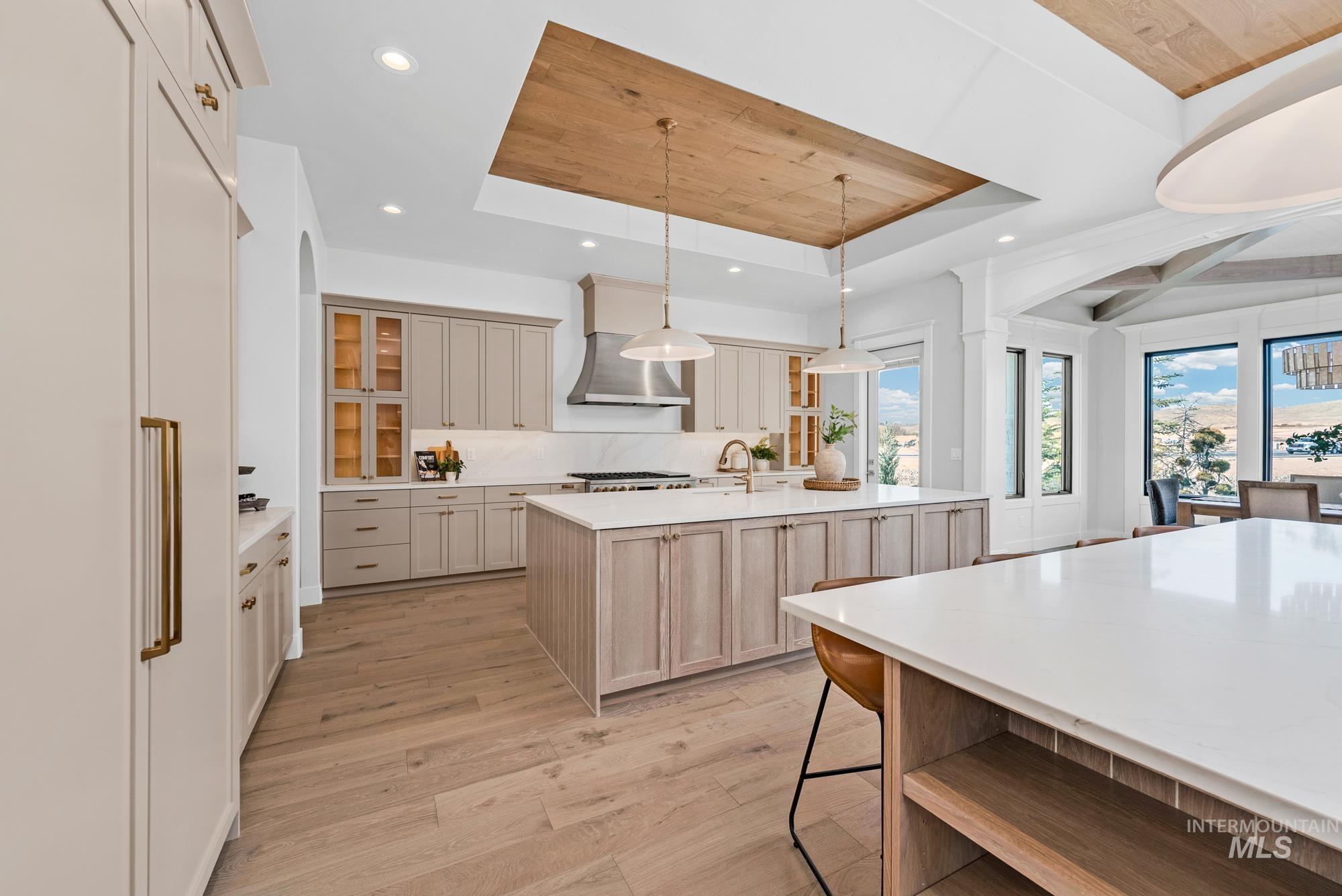 Kitchen featuring open shelves, a raised ceiling, pendant lighting, light wood-style flooring, and an island with sink