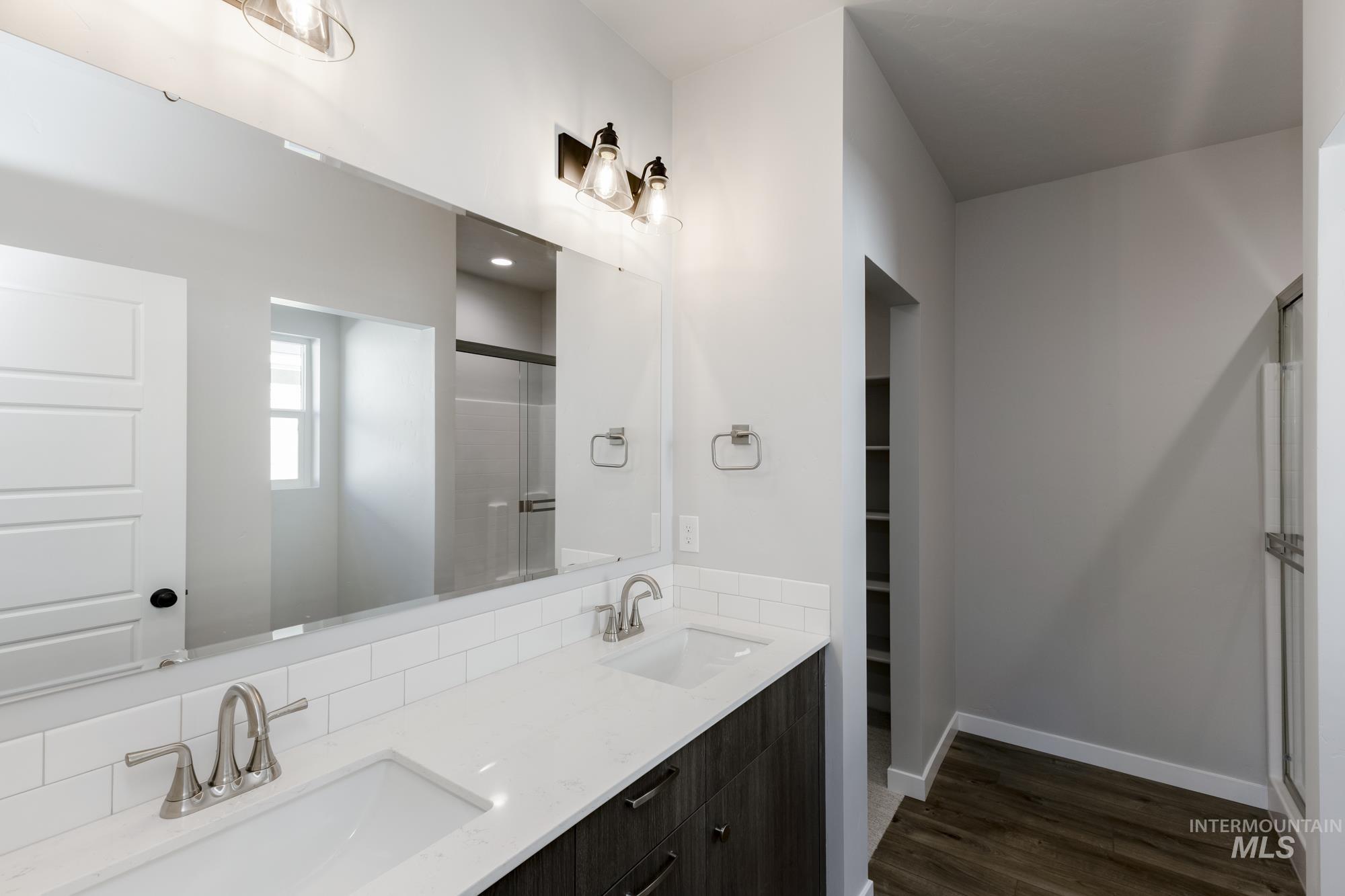 Bathroom with a stall shower, double vanity, dark wood-type flooring, and a walk in closet