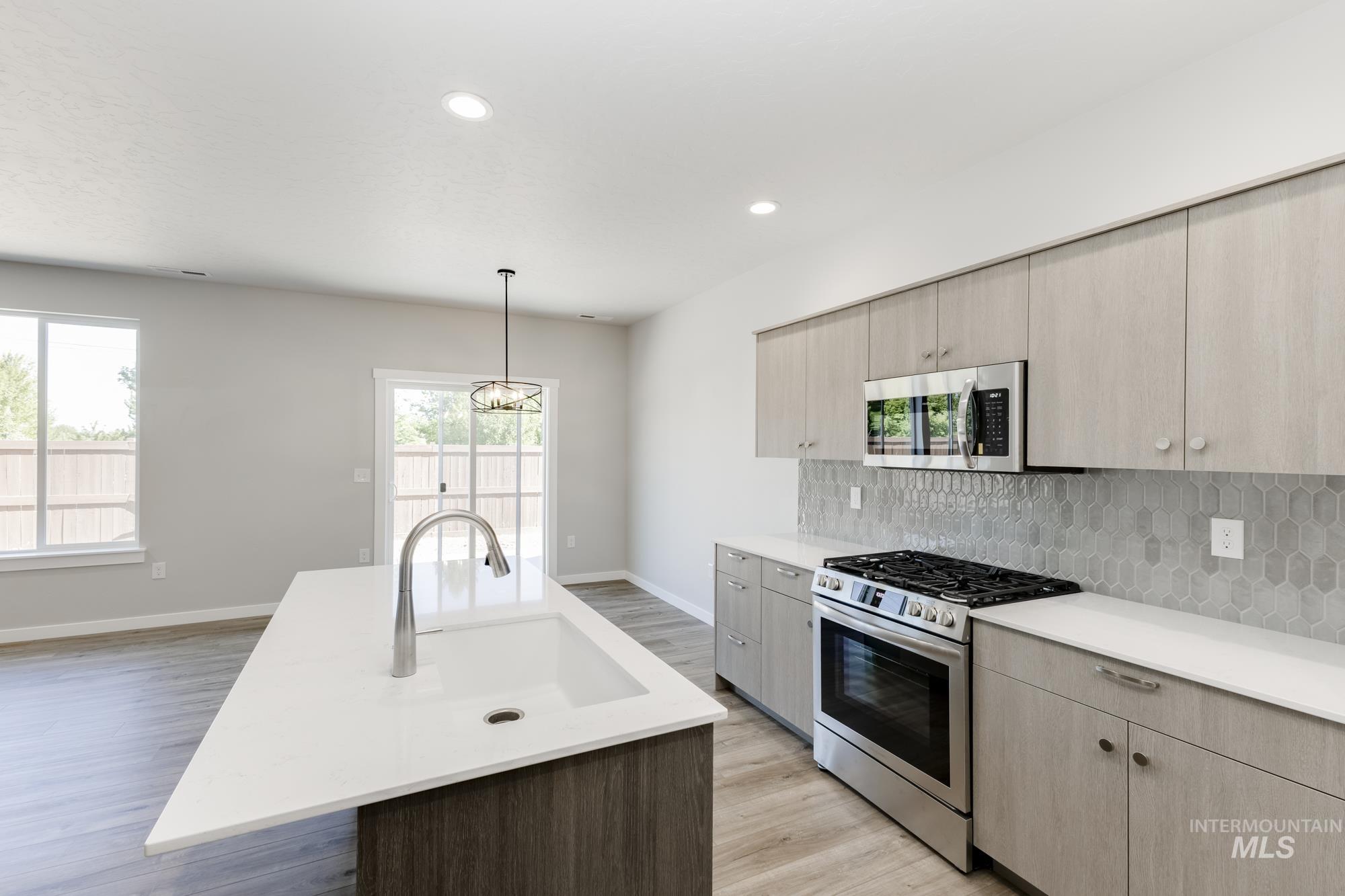 Kitchen with stainless steel appliances, light brown cabinetry, pendant lighting, light wood finished floors, and a center island with sink
