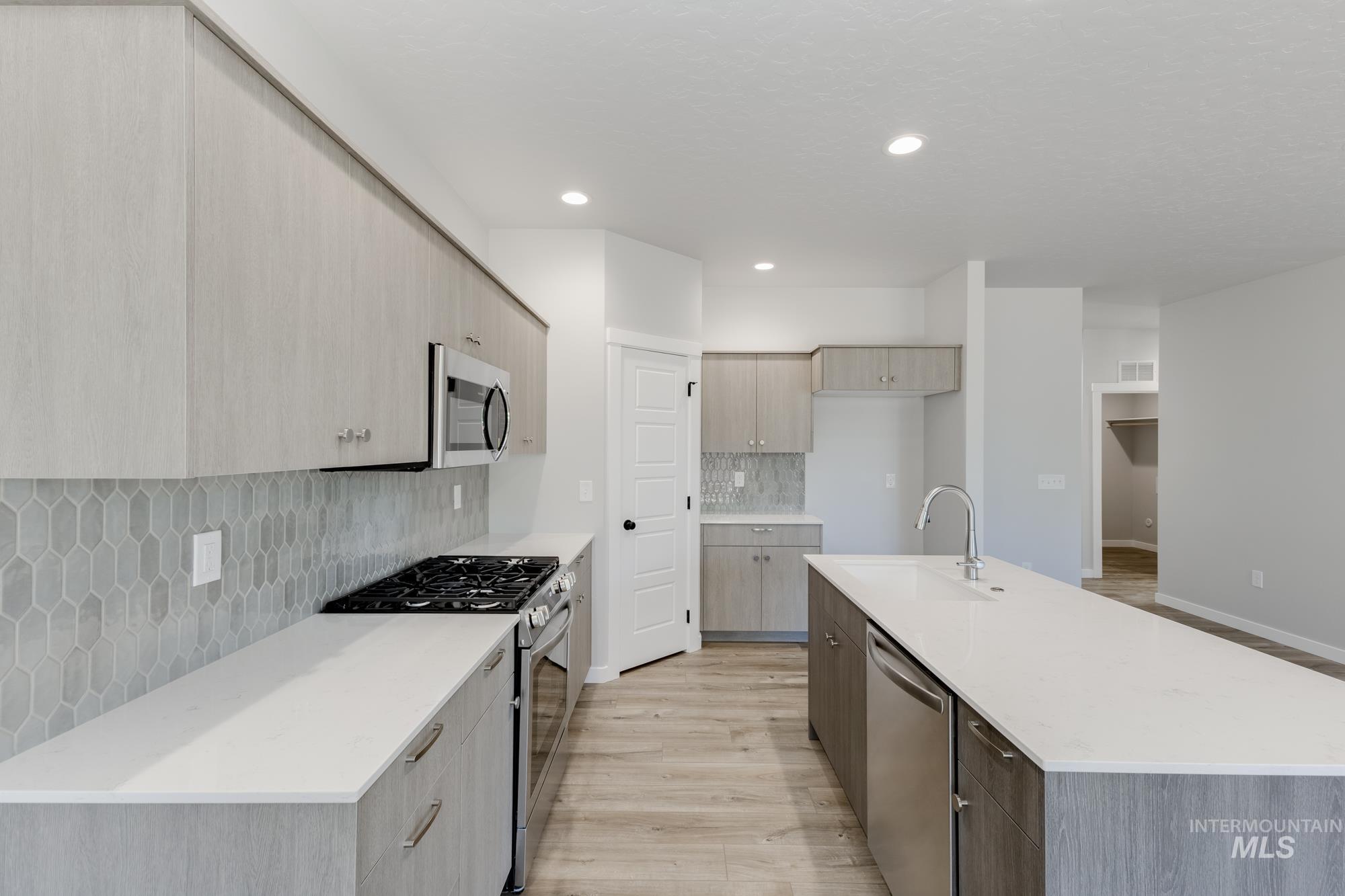 Kitchen featuring stainless steel appliances, tasteful backsplash, light stone counters, a kitchen island with sink, and modern cabinets
