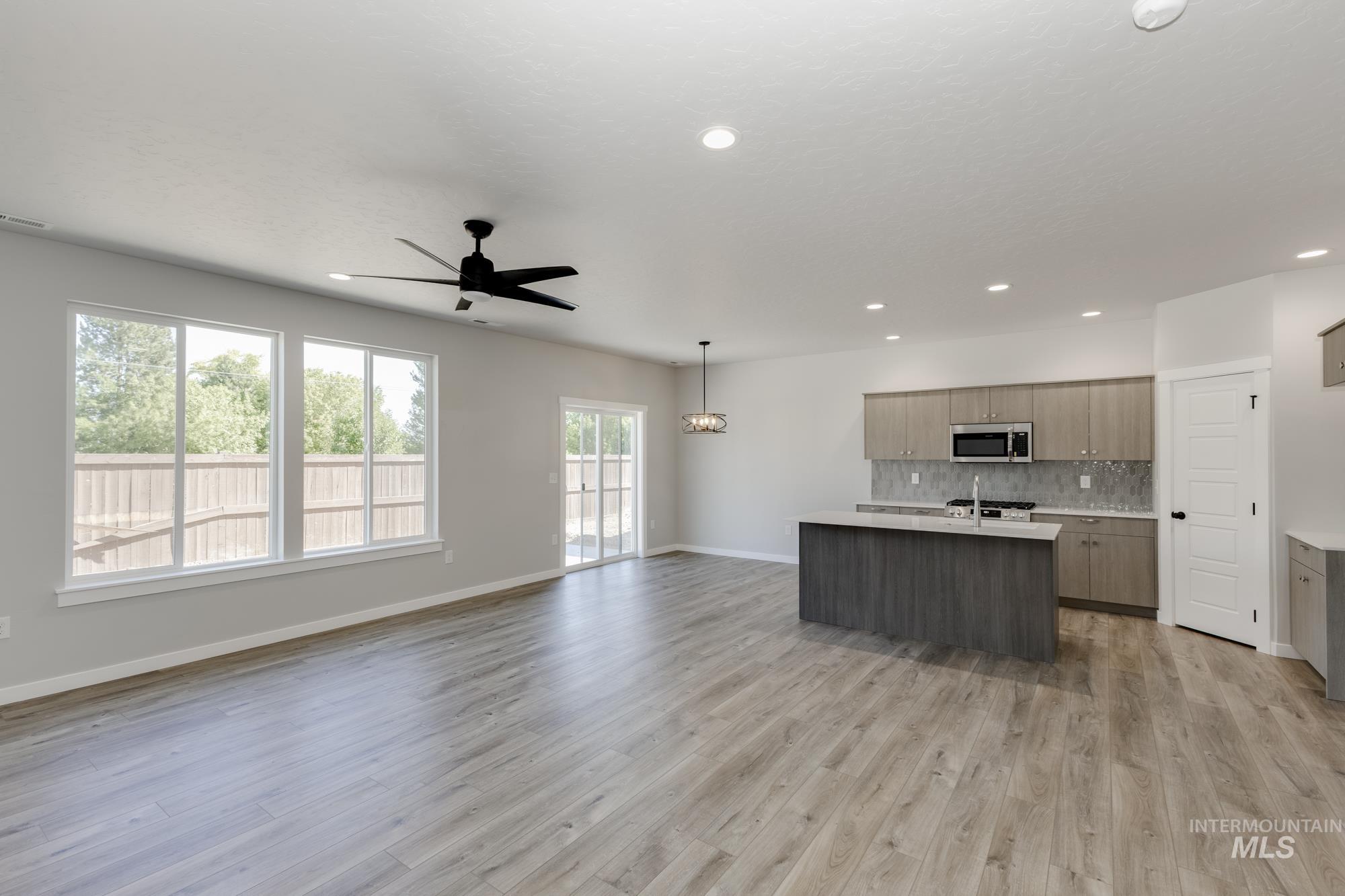 Kitchen featuring open floor plan, a kitchen island with sink, tasteful backsplash, decorative light fixtures, and light wood-style flooring