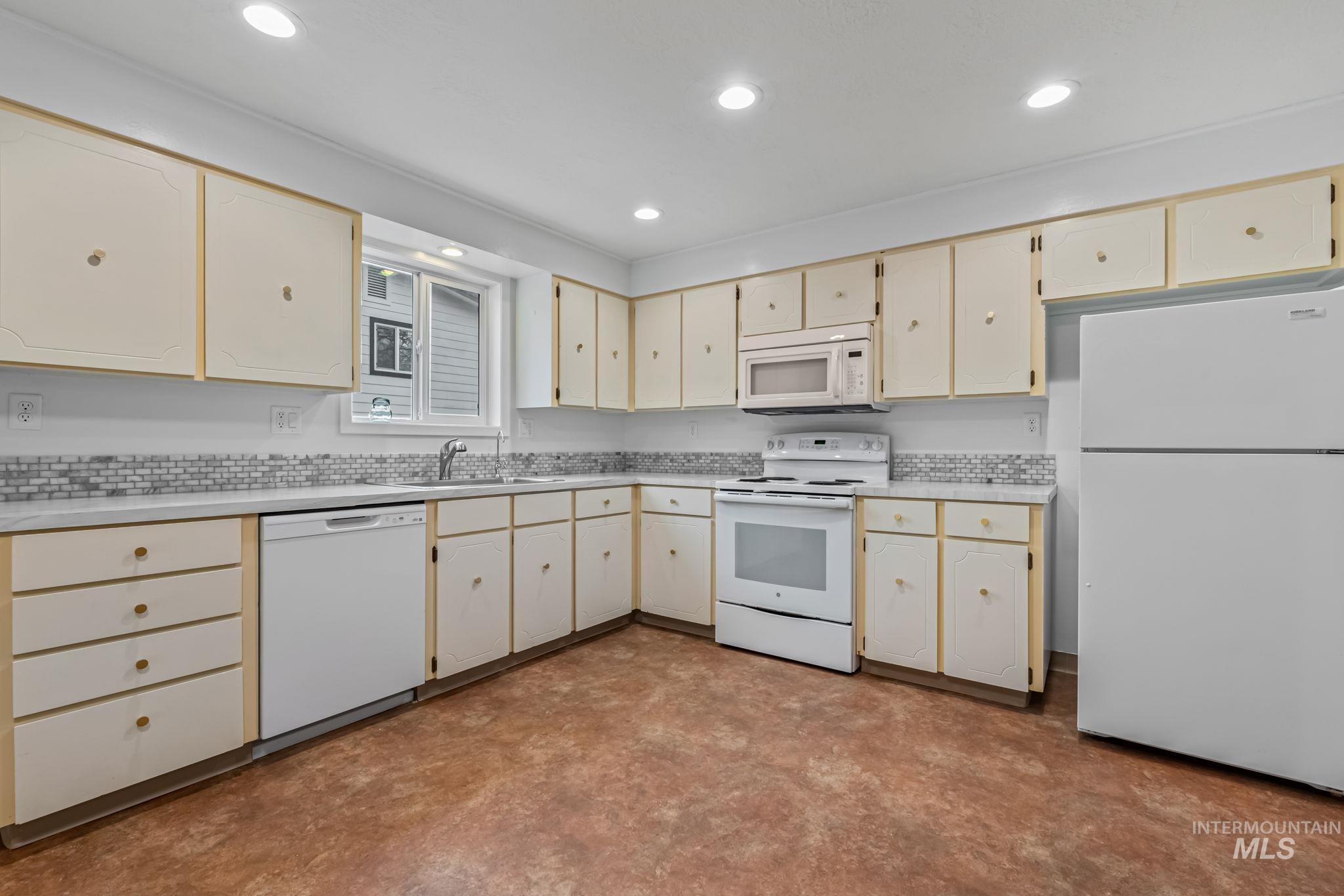 Kitchen featuring cream cabinets, white appliances, light countertops, and recessed lighting
