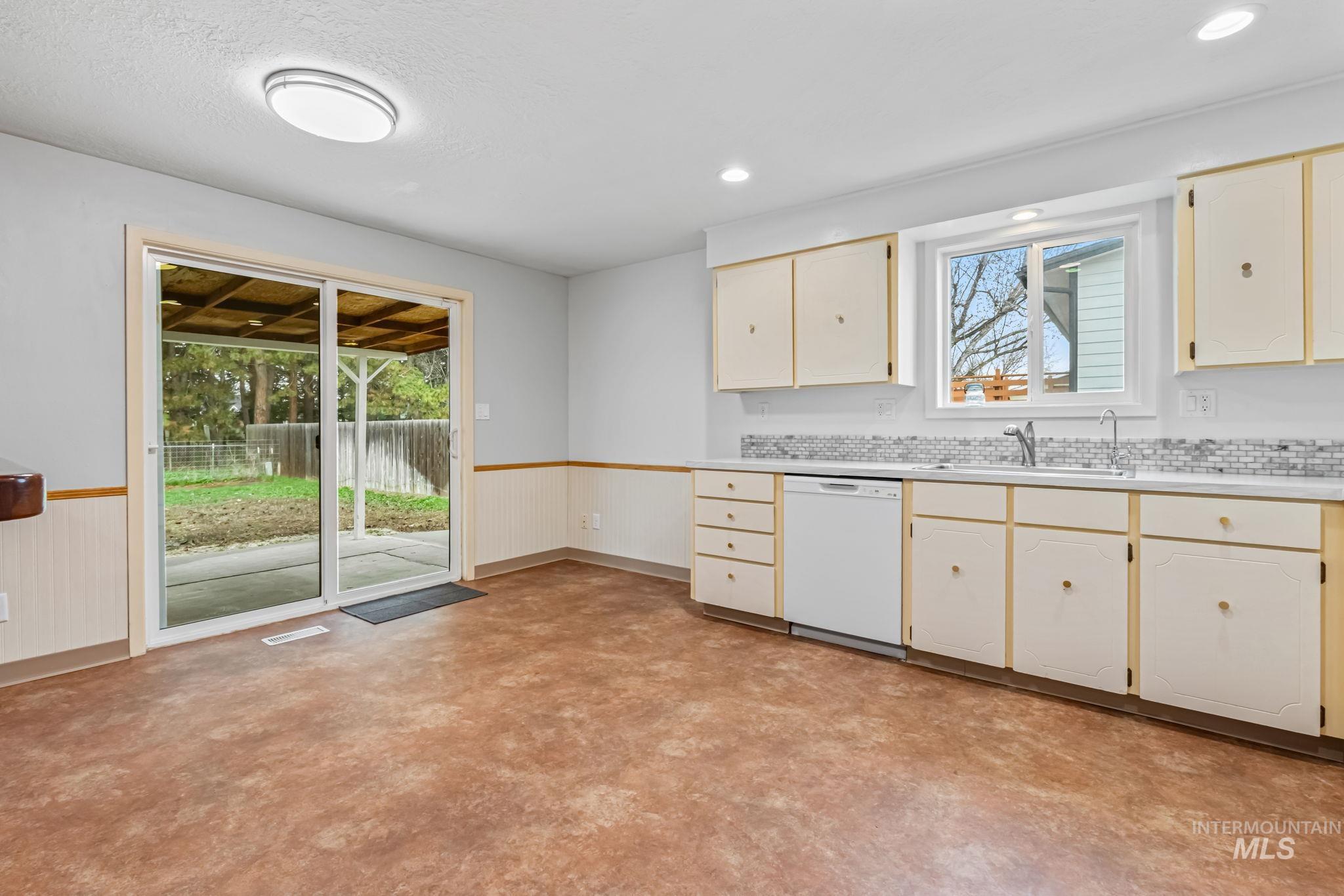 Kitchen featuring a wainscoted wall, light countertops, white dishwasher, and cream cabinetry