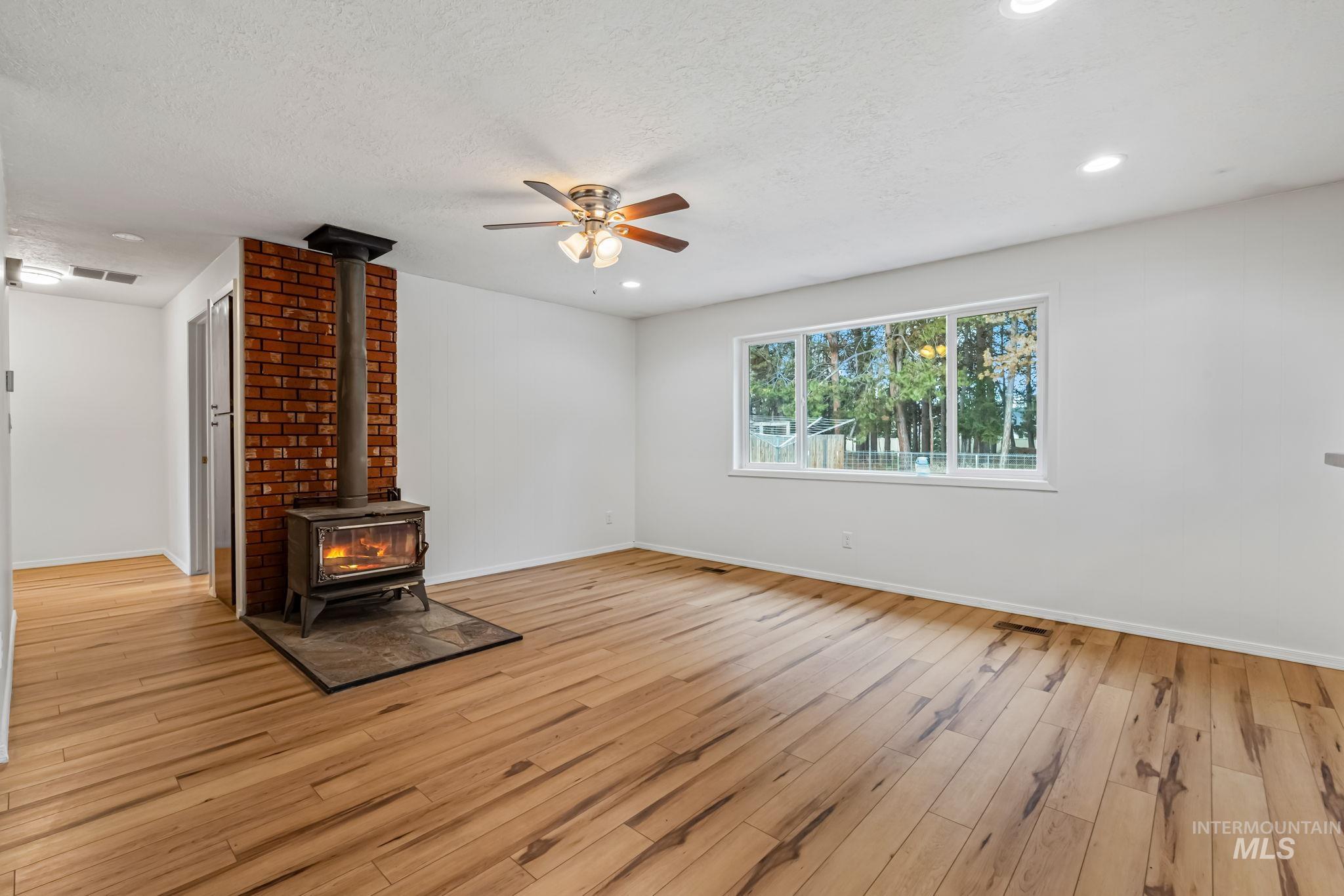 Unfurnished living room with a wood stove, light wood finished floors, a ceiling fan, recessed lighting, and a textured ceiling