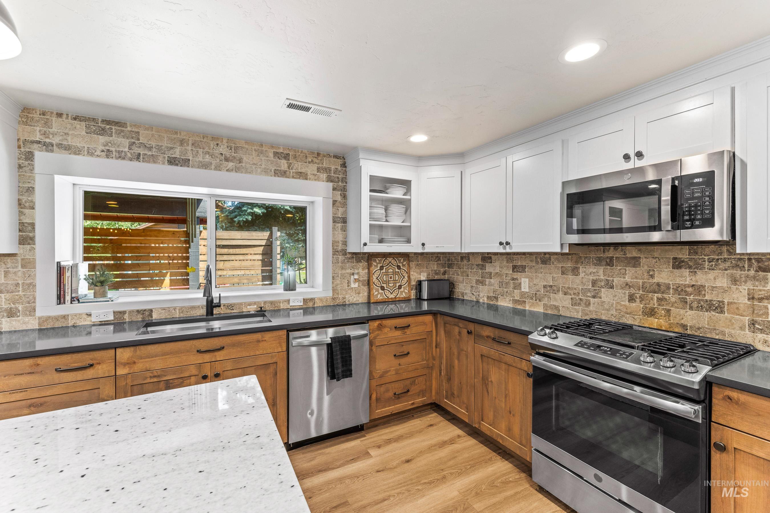 Kitchen featuring appliances with stainless steel finishes, light wood-type flooring, white cabinetry, backsplash, and recessed lighting