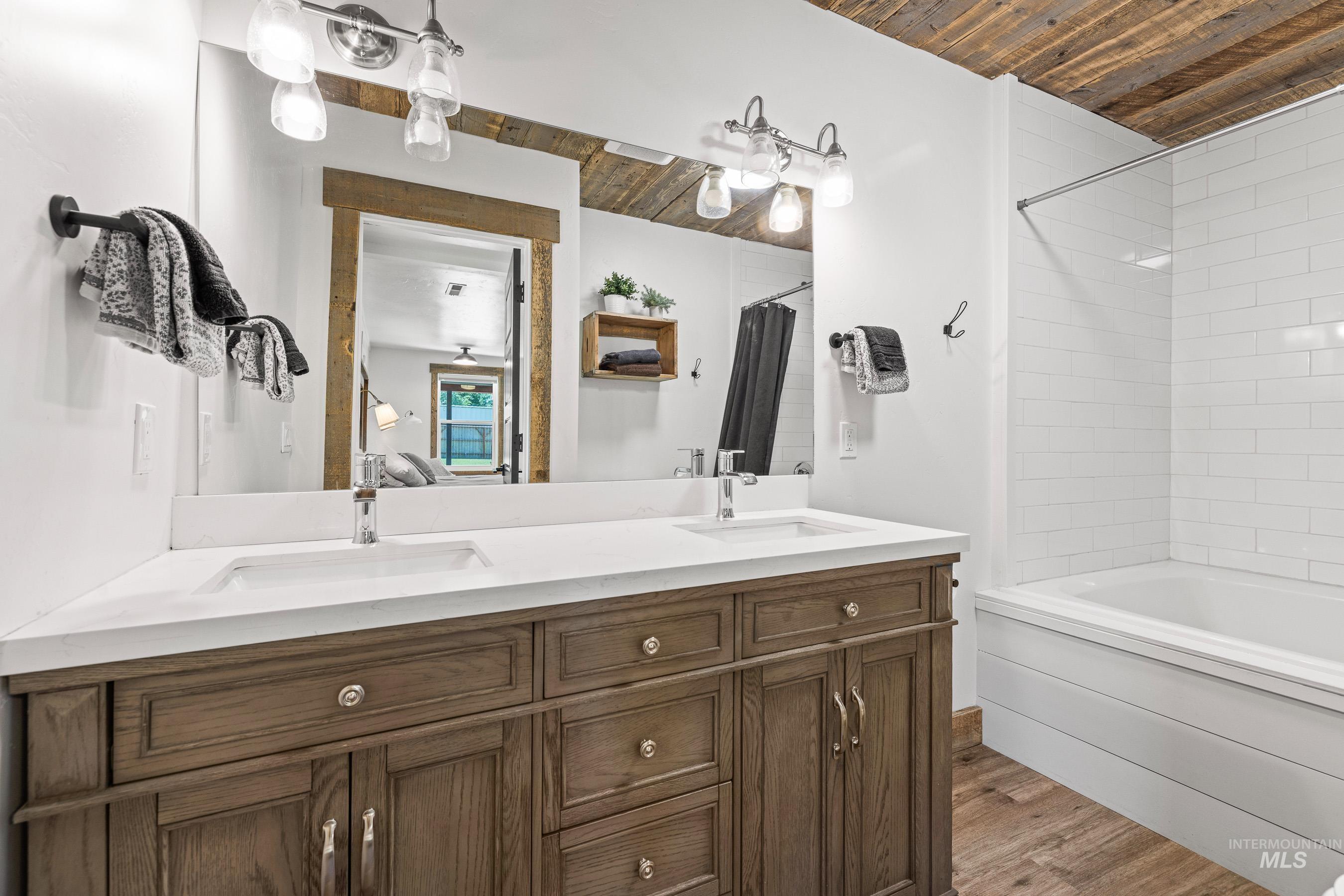 Bathroom with wood ceiling, double vanity, shower / tub combo with curtain, and wood finished floors