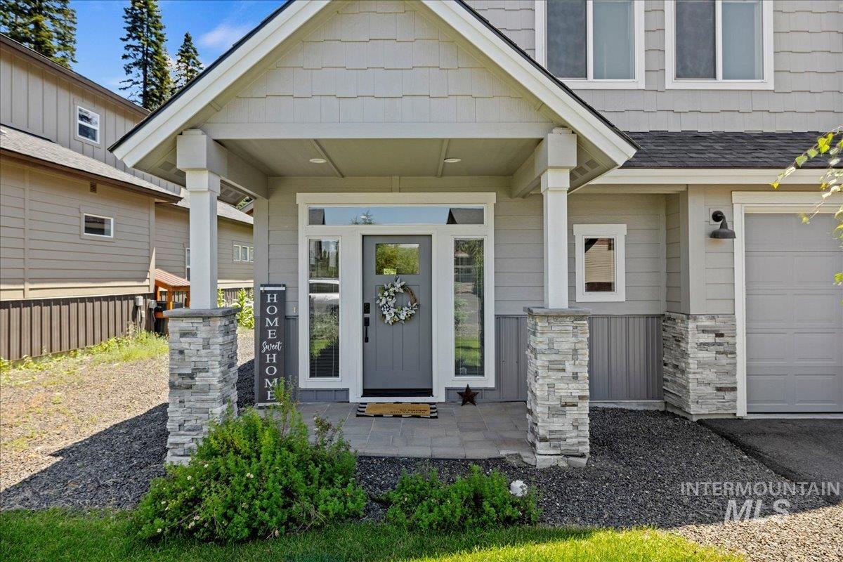 Doorway to property with a garage, covered porch, and roof with shingles