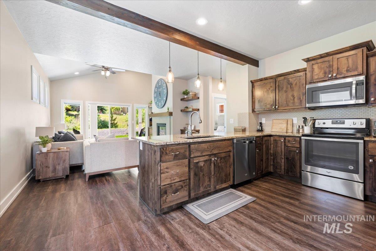 Kitchen with stainless steel appliances, a peninsula, dark wood-type flooring, light stone counters, and recessed lighting