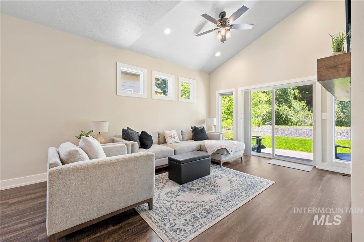 Living room with a ceiling fan, high vaulted ceiling, dark wood-type flooring, and recessed lighting