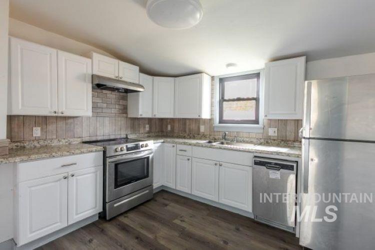 Kitchen with stainless steel appliances, white cabinets, dark wood-type flooring, under cabinet range hood, and decorative backsplash