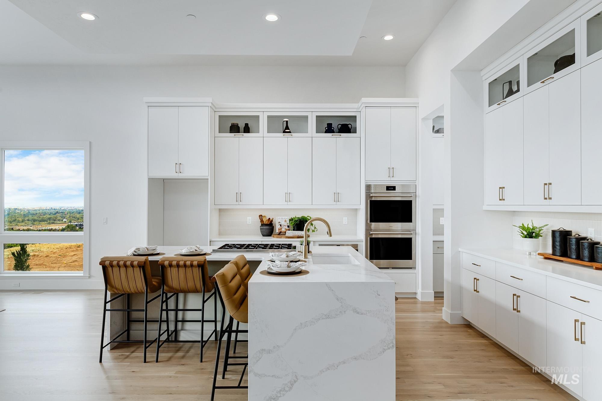 Kitchen with white cabinets, light wood finished floors, light stone counters, recessed lighting, and a breakfast bar area