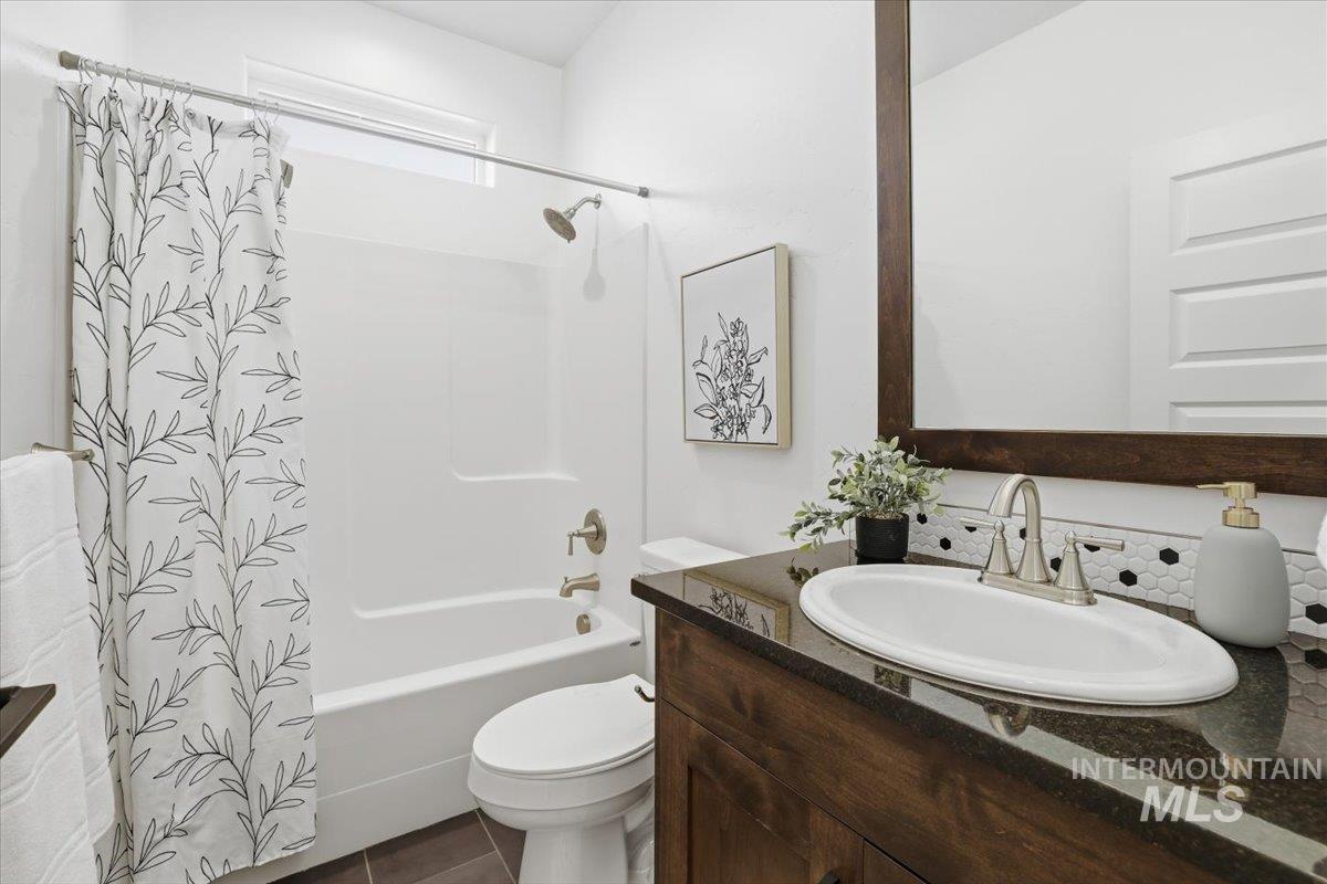 Bathroom featuring vanity, shower / bath combo with shower curtain, and dark tile patterned flooring
