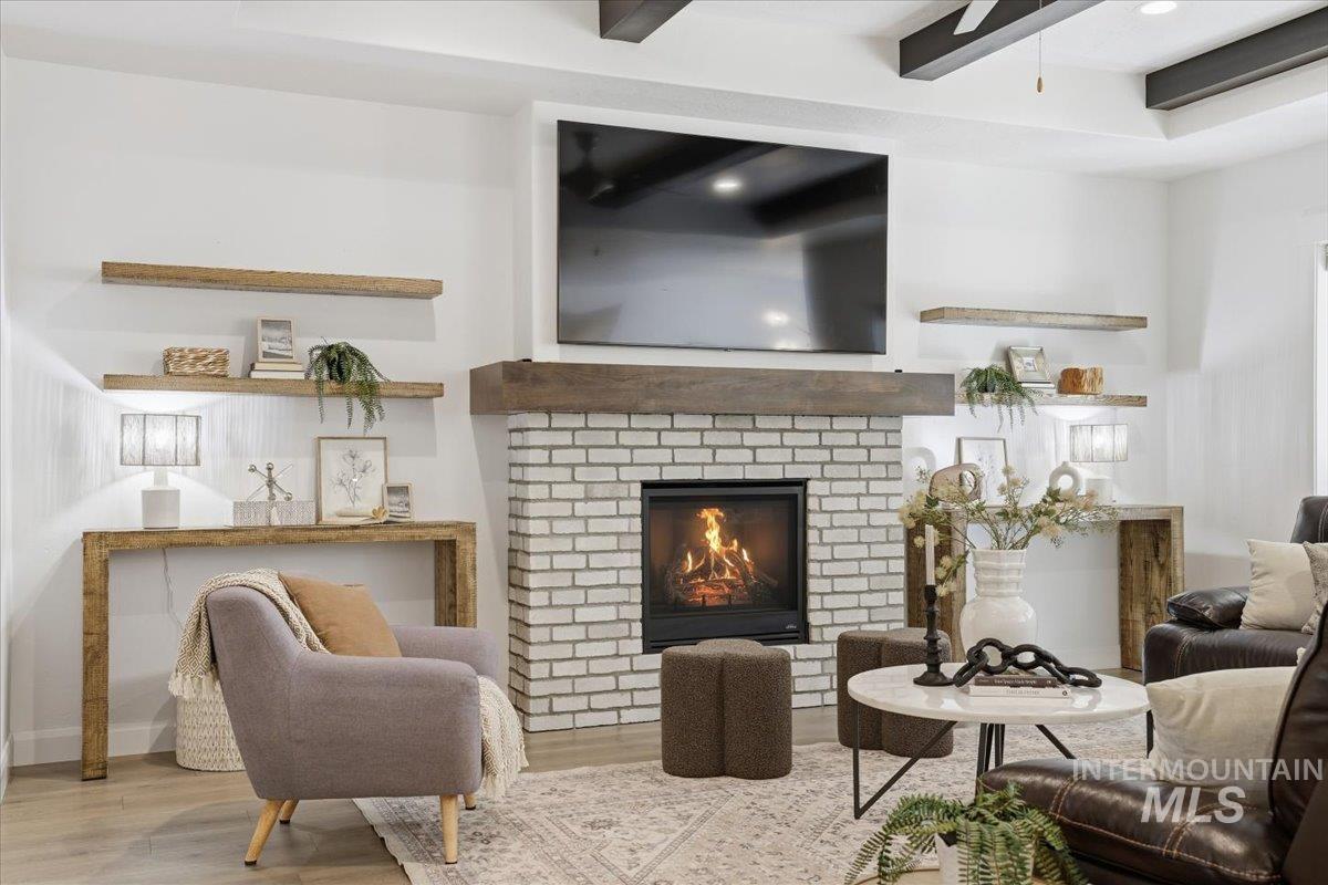 Living area featuring a fireplace, wood finished floors, beam ceiling, and ceiling fan