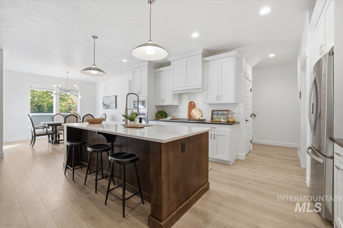 Kitchen with white cabinets, a breakfast bar area, a kitchen island with sink, light wood-style flooring, and a textured ceiling