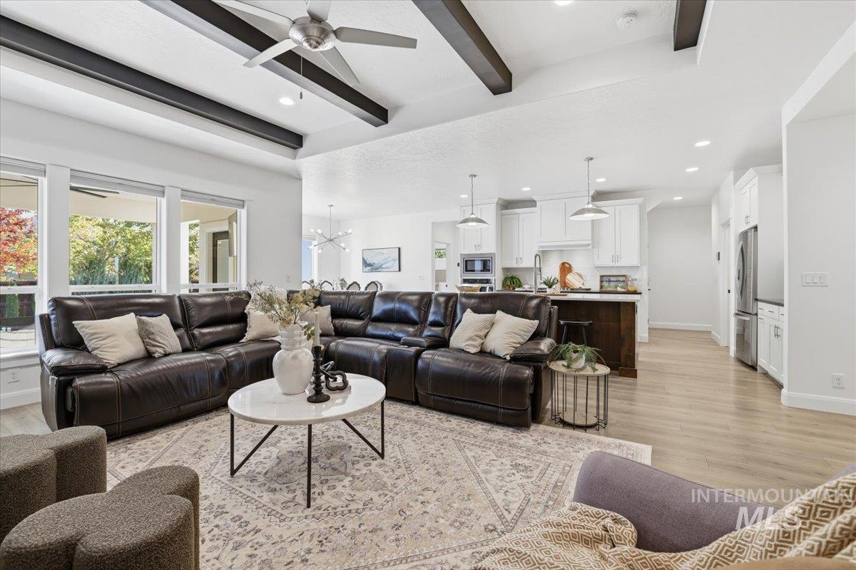 Living room with beamed ceiling, light wood-style flooring, a chandelier, a ceiling fan, and recessed lighting