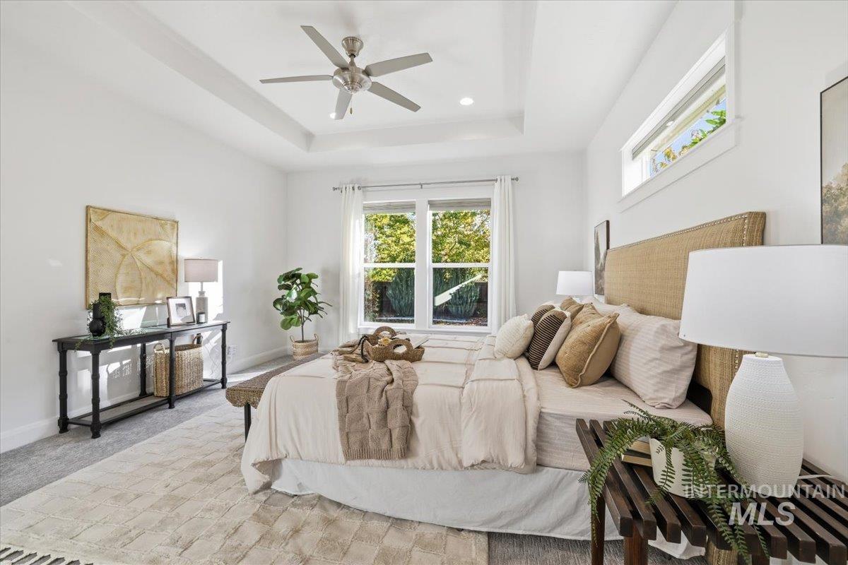 Bedroom with a raised ceiling, carpet flooring, and a ceiling fan