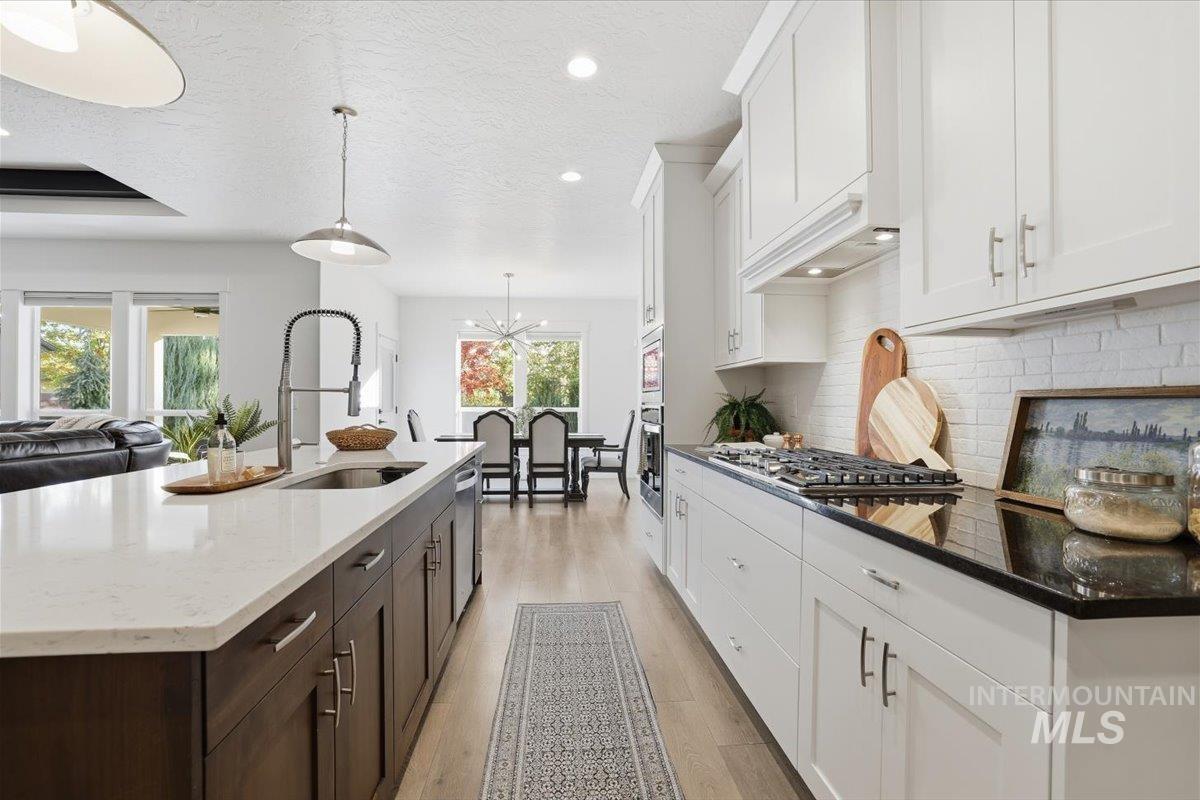 Kitchen featuring white cabinets, light wood-style floors, a textured ceiling, decorative backsplash, and pendant lighting