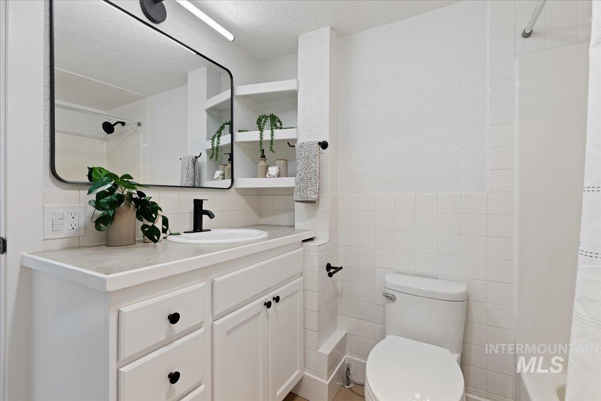 Full bathroom featuring tile walls, vanity, a textured ceiling, and shower / bathtub combination with curtain