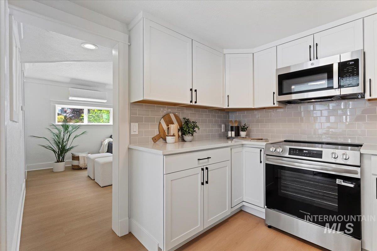 Kitchen featuring stainless steel appliances, white cabinetry, light wood finished floors, tasteful backsplash, and light stone countertops