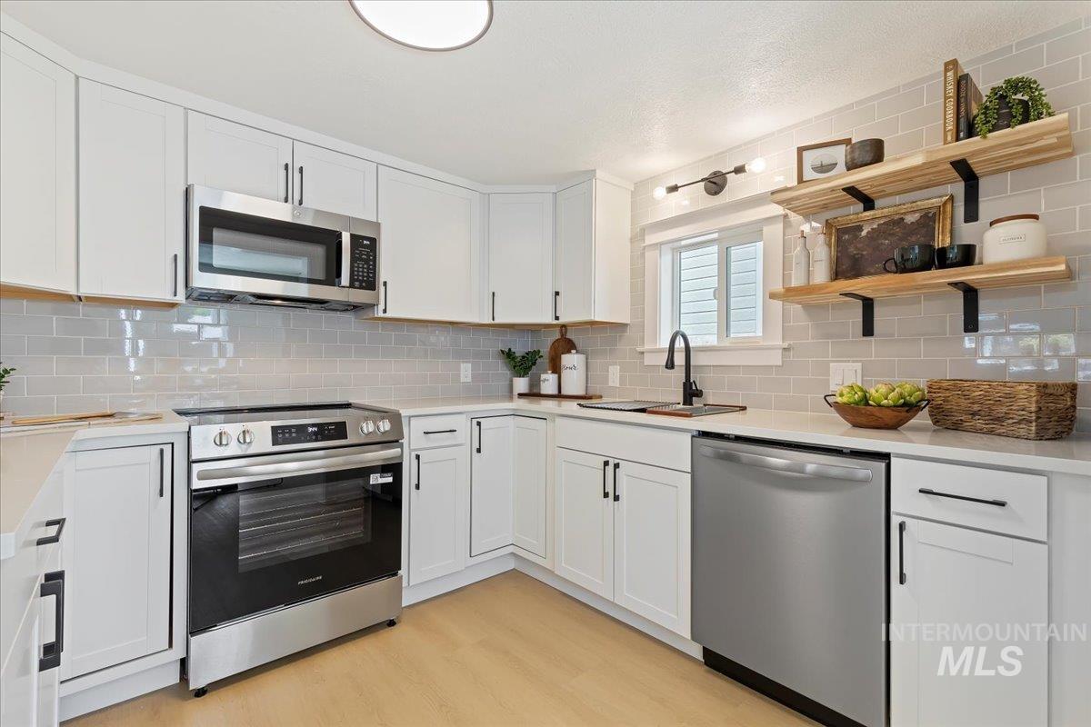 Kitchen with appliances with stainless steel finishes, white cabinetry, backsplash, light wood-style floors, and open shelves
