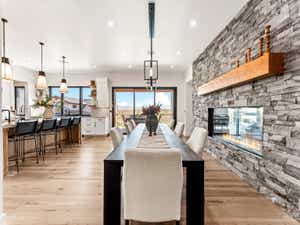 Open-concept living space featuring light wood-finish flooring, a long linear fireplace with a stone-clad wall and wood mantel, a large kitchen island with pendant lighting, and expansive sliding glass doors