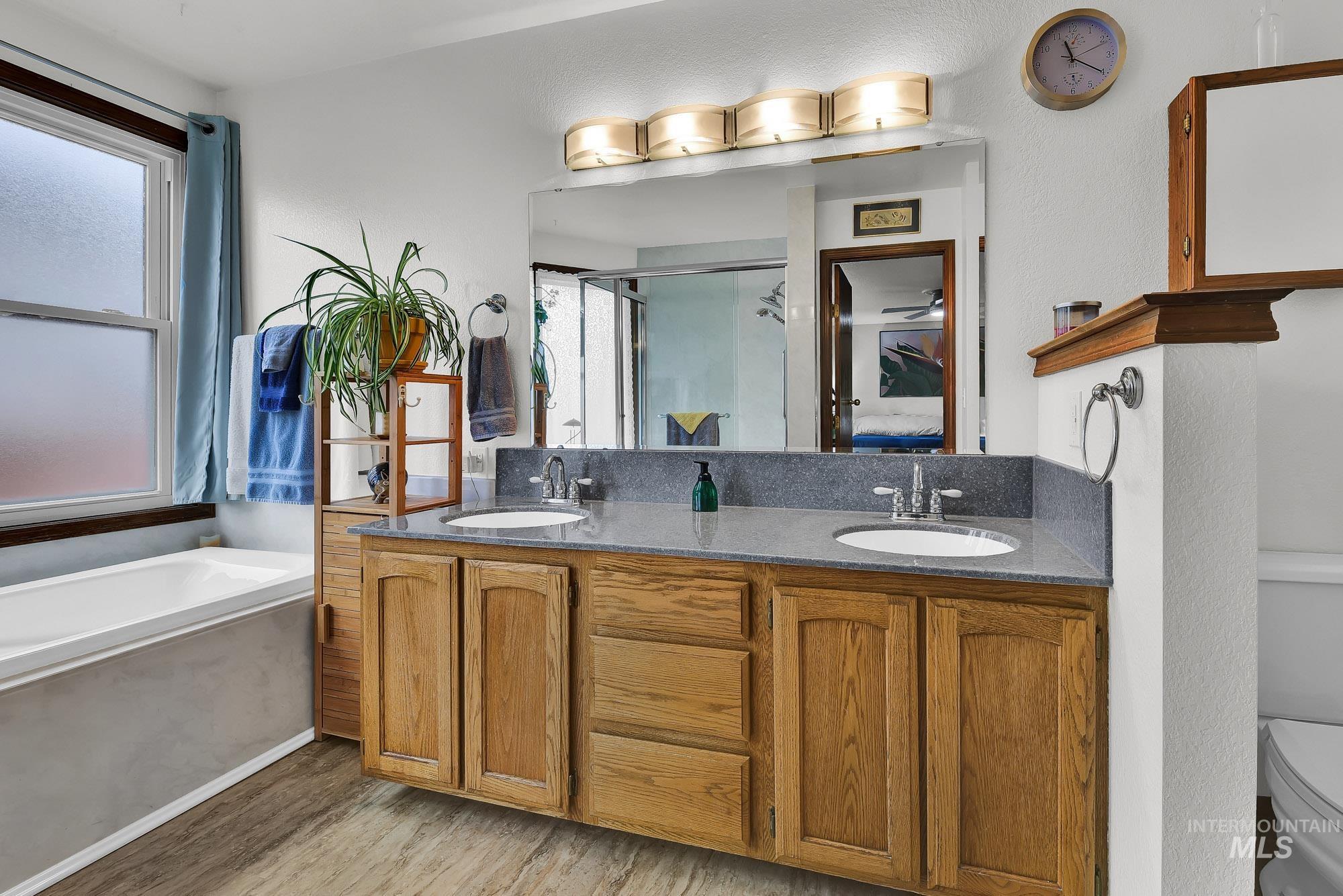 Ensuite bathroom with double vanity, a garden tub, a shower stall, and light wood finished floors