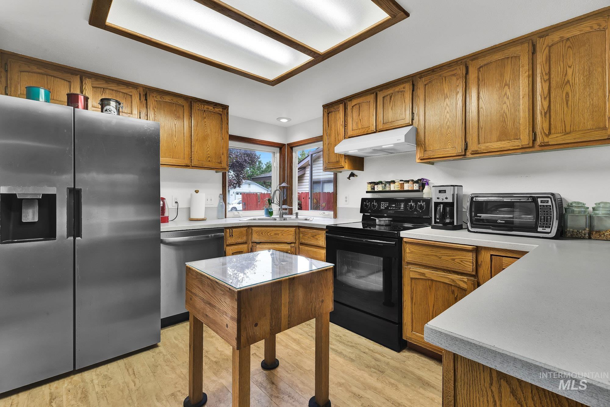 Kitchen with appliances with stainless steel finishes, brown cabinetry, light countertops, light wood-type flooring, and under cabinet range hood