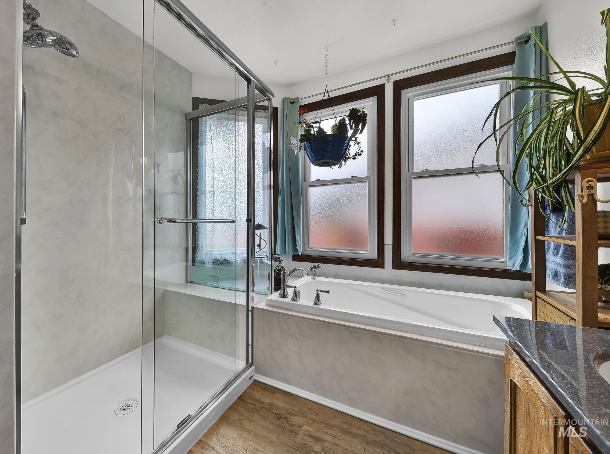 Full bathroom featuring vanity, a garden tub, a shower stall, and wood finished floors