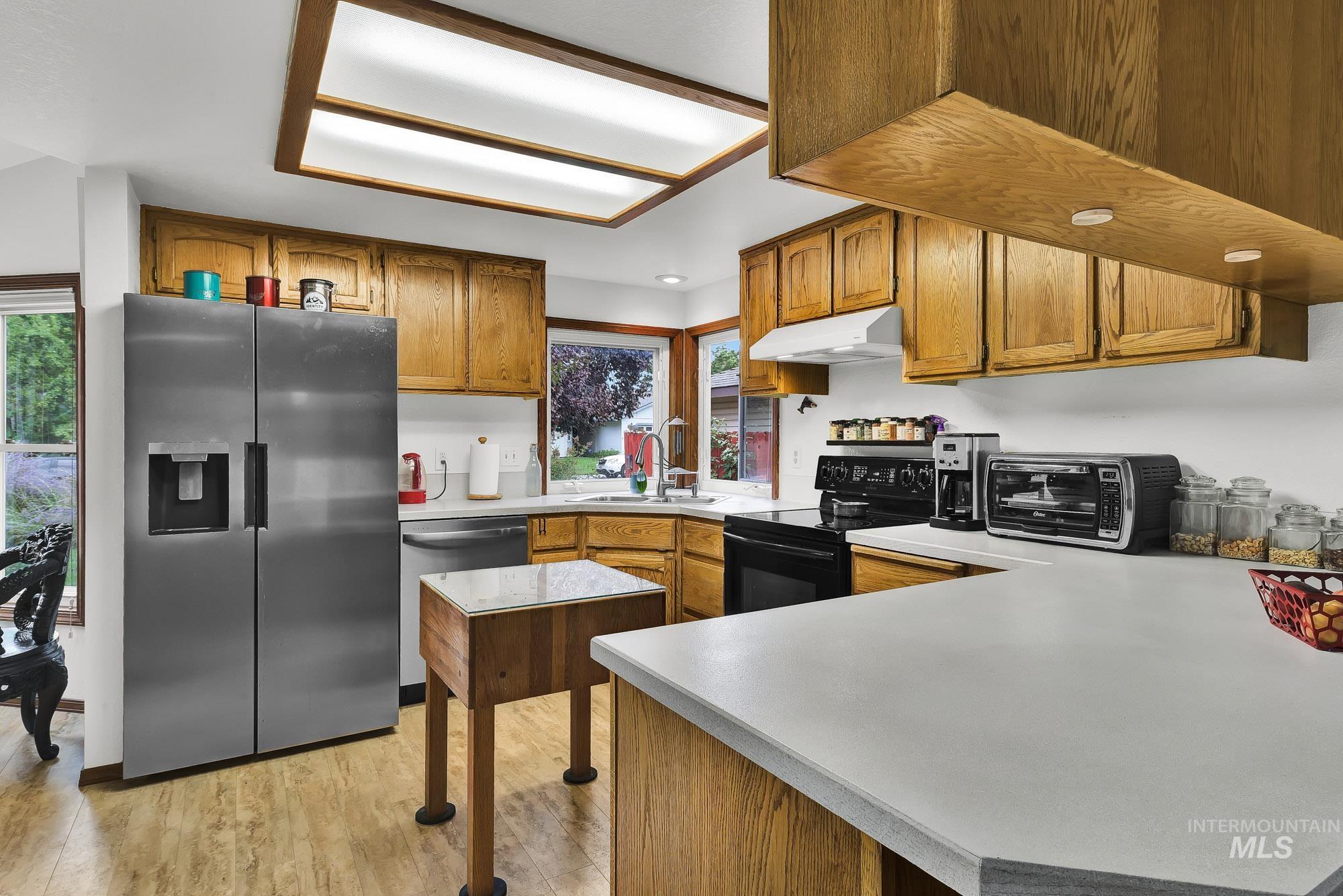 Kitchen featuring appliances with stainless steel finishes, brown cabinets, light wood-style floors, and light countertops