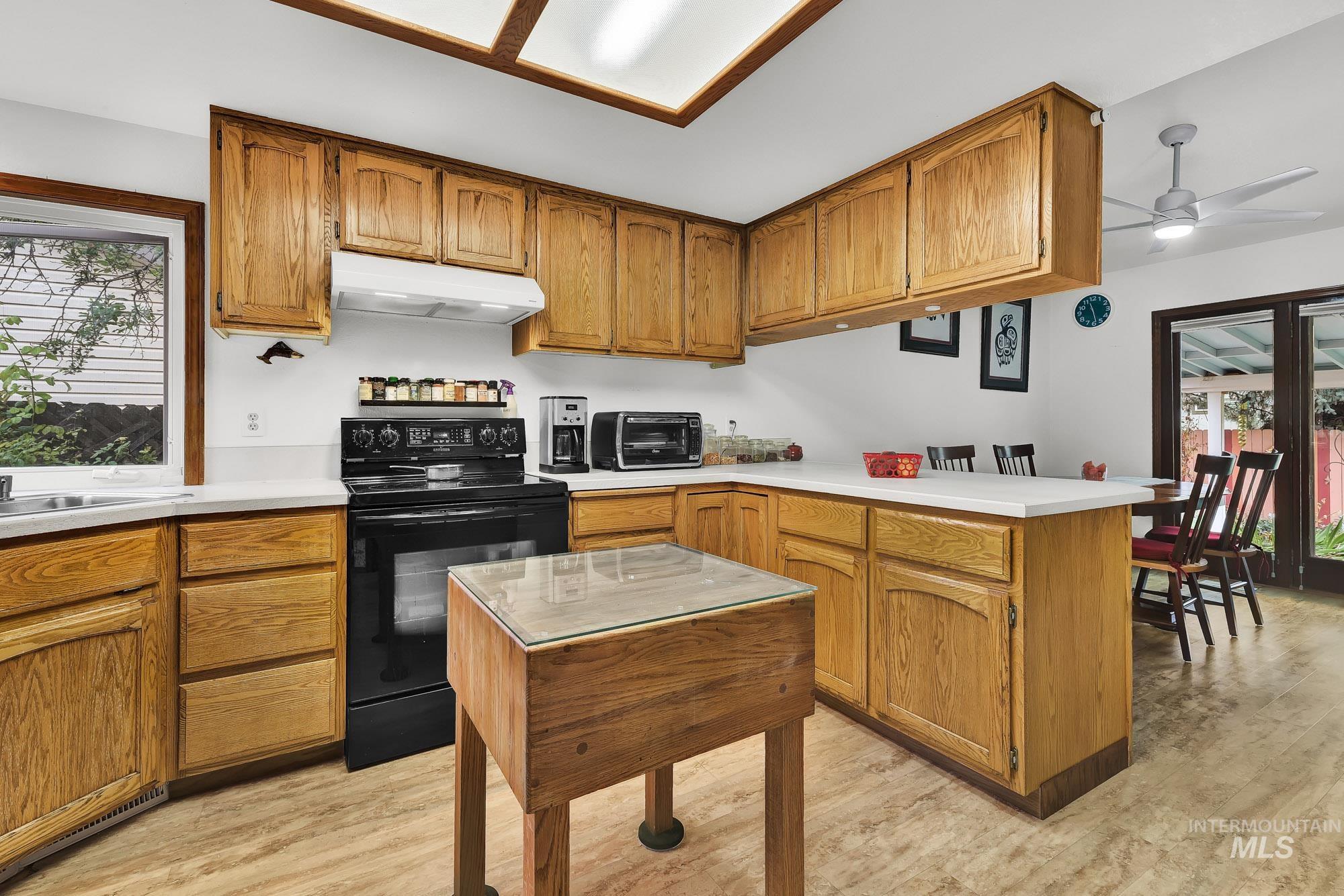 Kitchen featuring a peninsula, brown cabinetry, black electric range, light wood-style floors, and light countertops