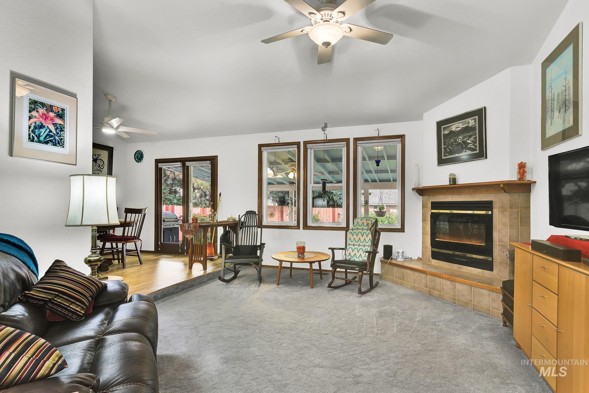 Living room featuring healthy amount of natural light, a ceiling fan, a tiled fireplace, lofted ceiling, and light colored carpet
