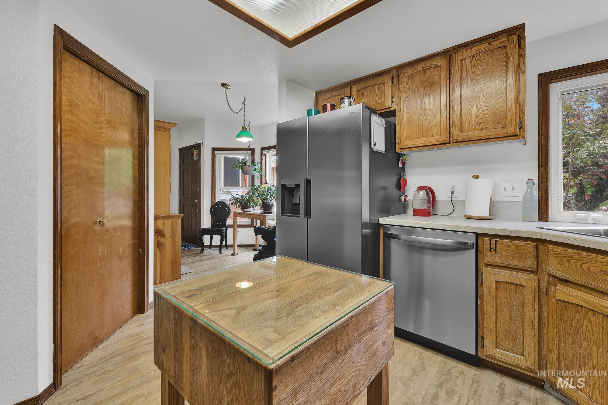 Kitchen with brown cabinets, appliances with stainless steel finishes, light wood finished floors, hanging light fixtures, and healthy amount of natural light